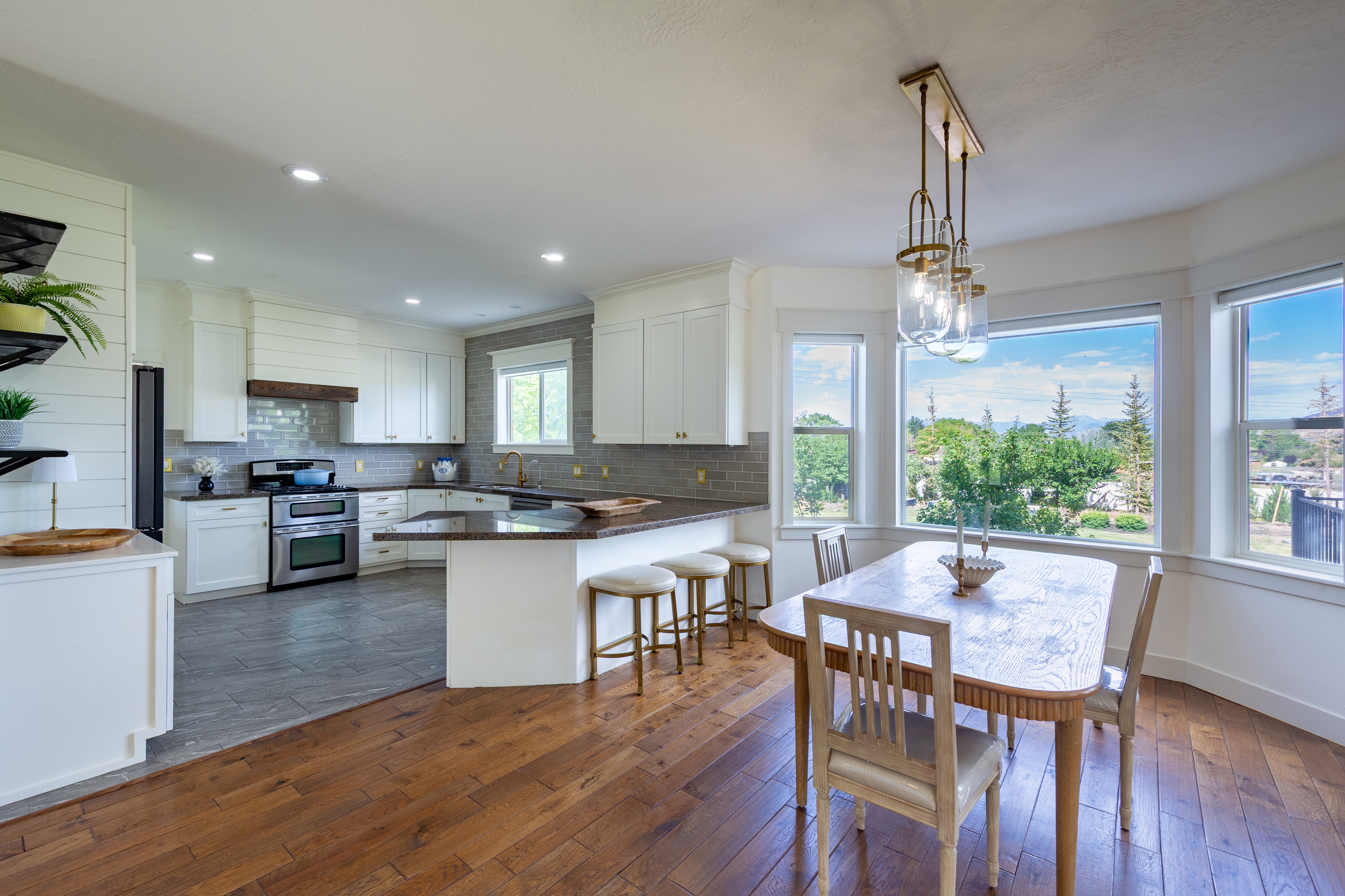Bright kitchen and dining area featuring hardwood flooring, white cabinetry, stainless steel appliances, a tile backsplash, and a breakfast bar