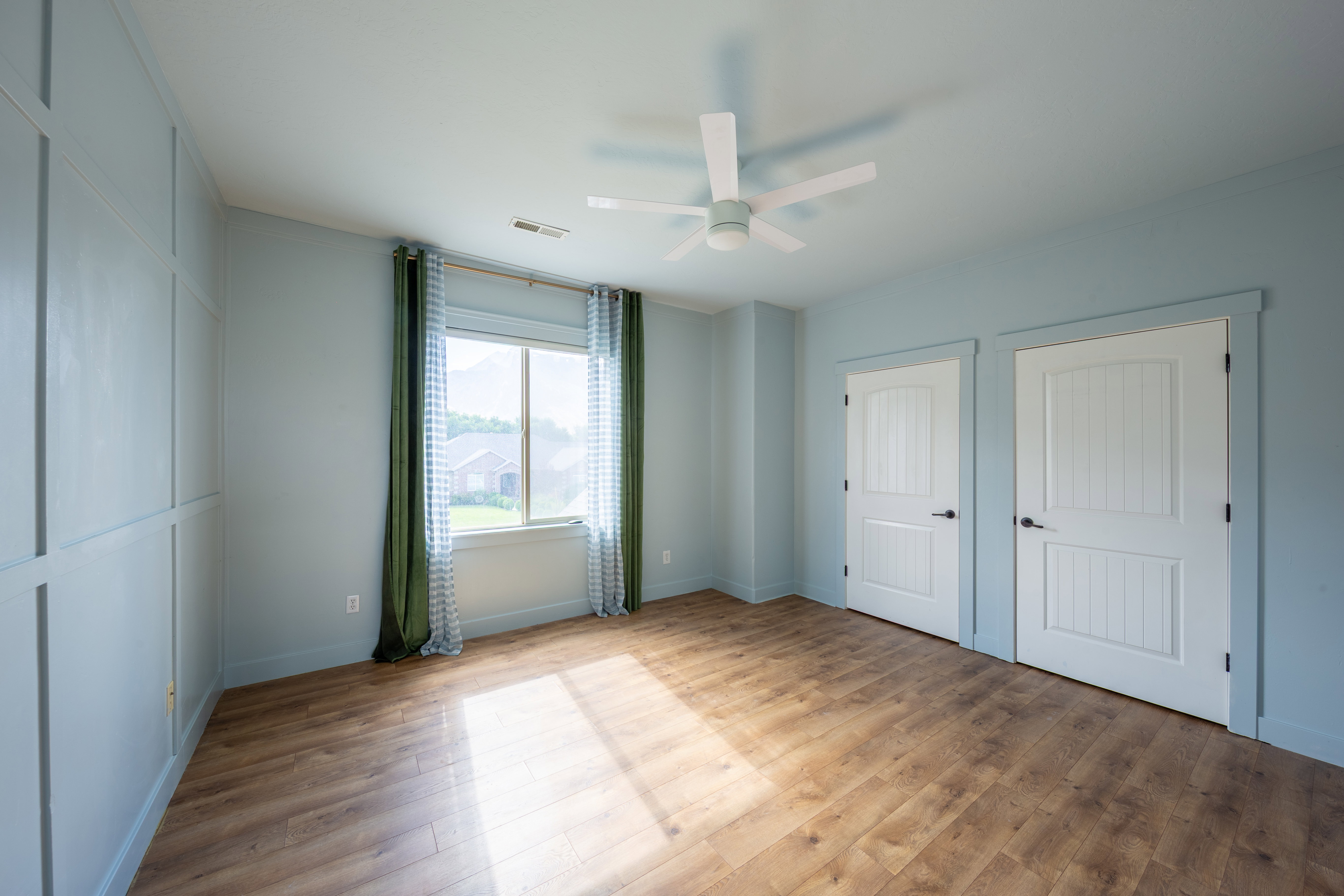 Spacious interior room featuring wood-finish flooring, a ceiling fan, and a large window