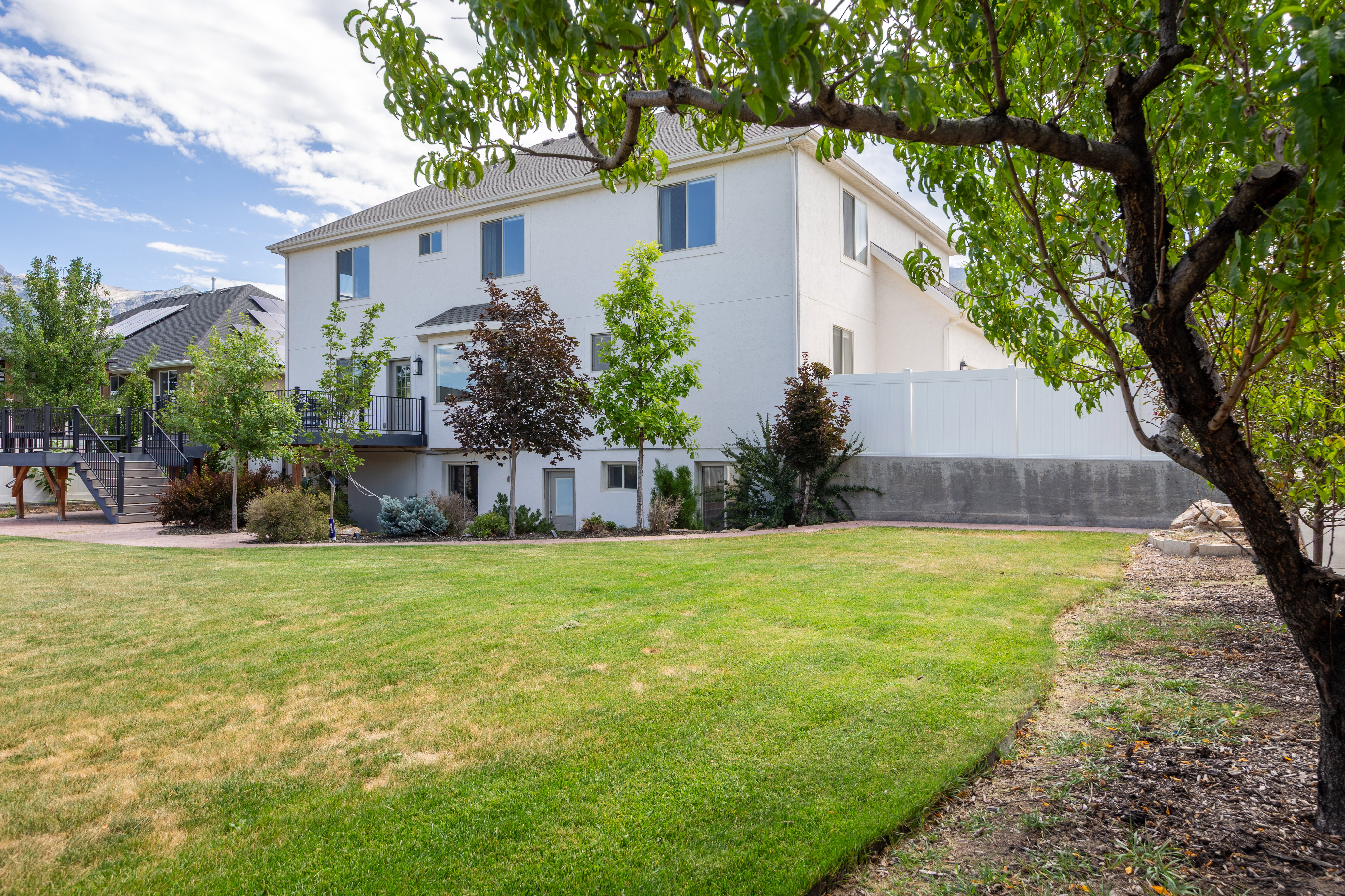 Spacious backyard featuring a large green lawn, mature trees, and a white privacy fence