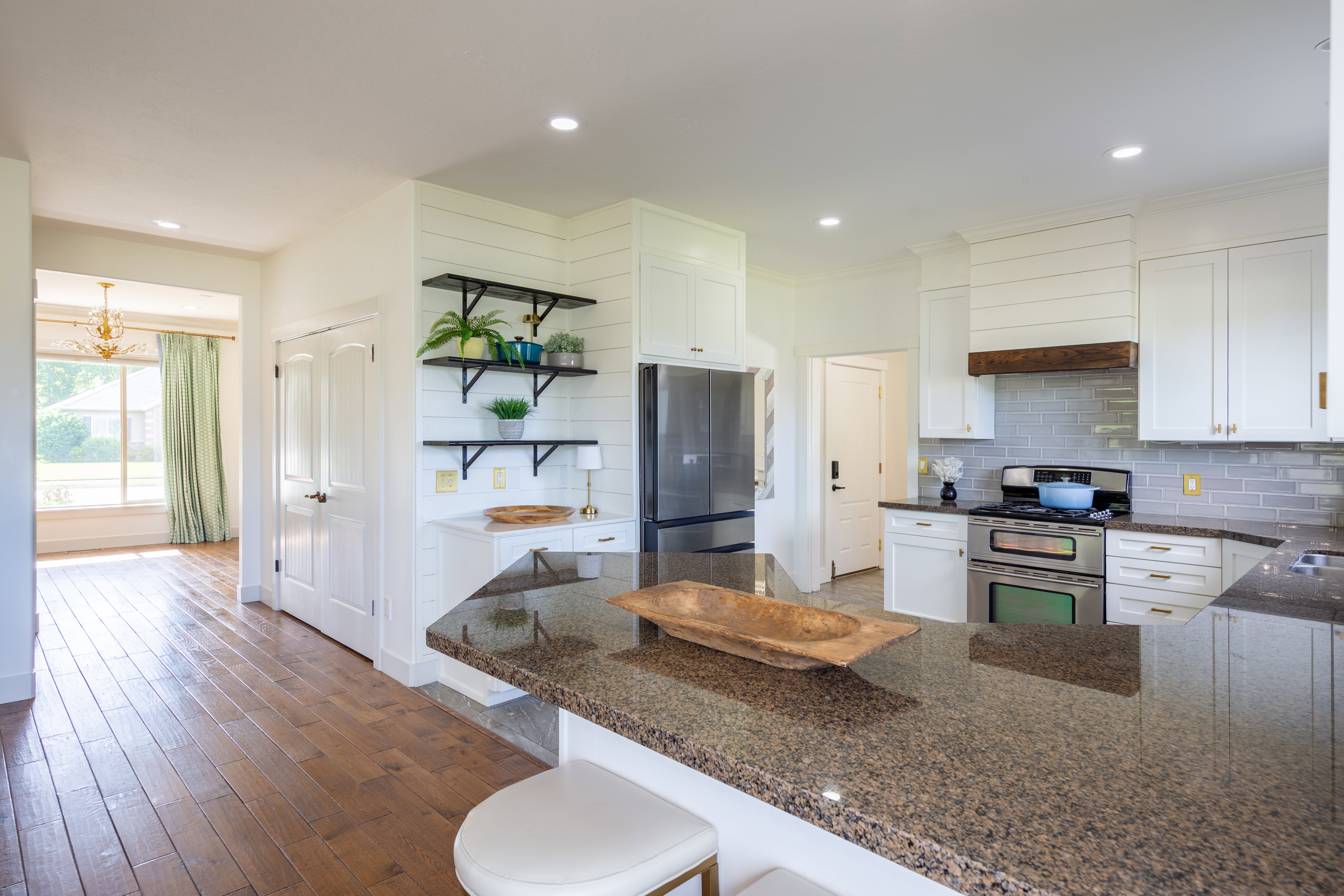Kitchen featuring an expansive island with a granite-style countertop, stainless steel appliances, white cabinetry with gold-tone hardware, a subway tile backsplash, and wood-finish flooring