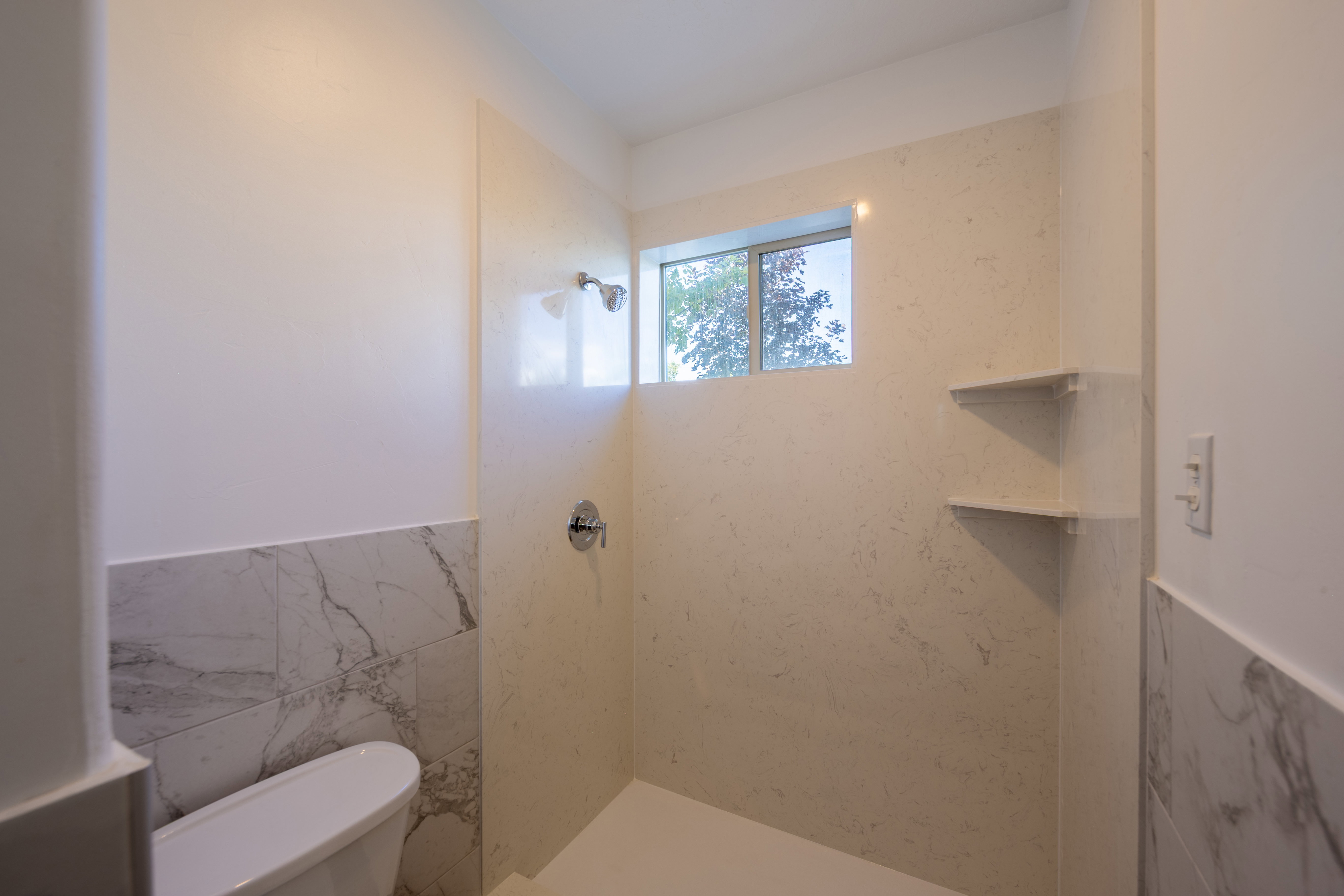 Walk-in shower featuring a chrome showerhead, a recessed window, and two corner storage shelves