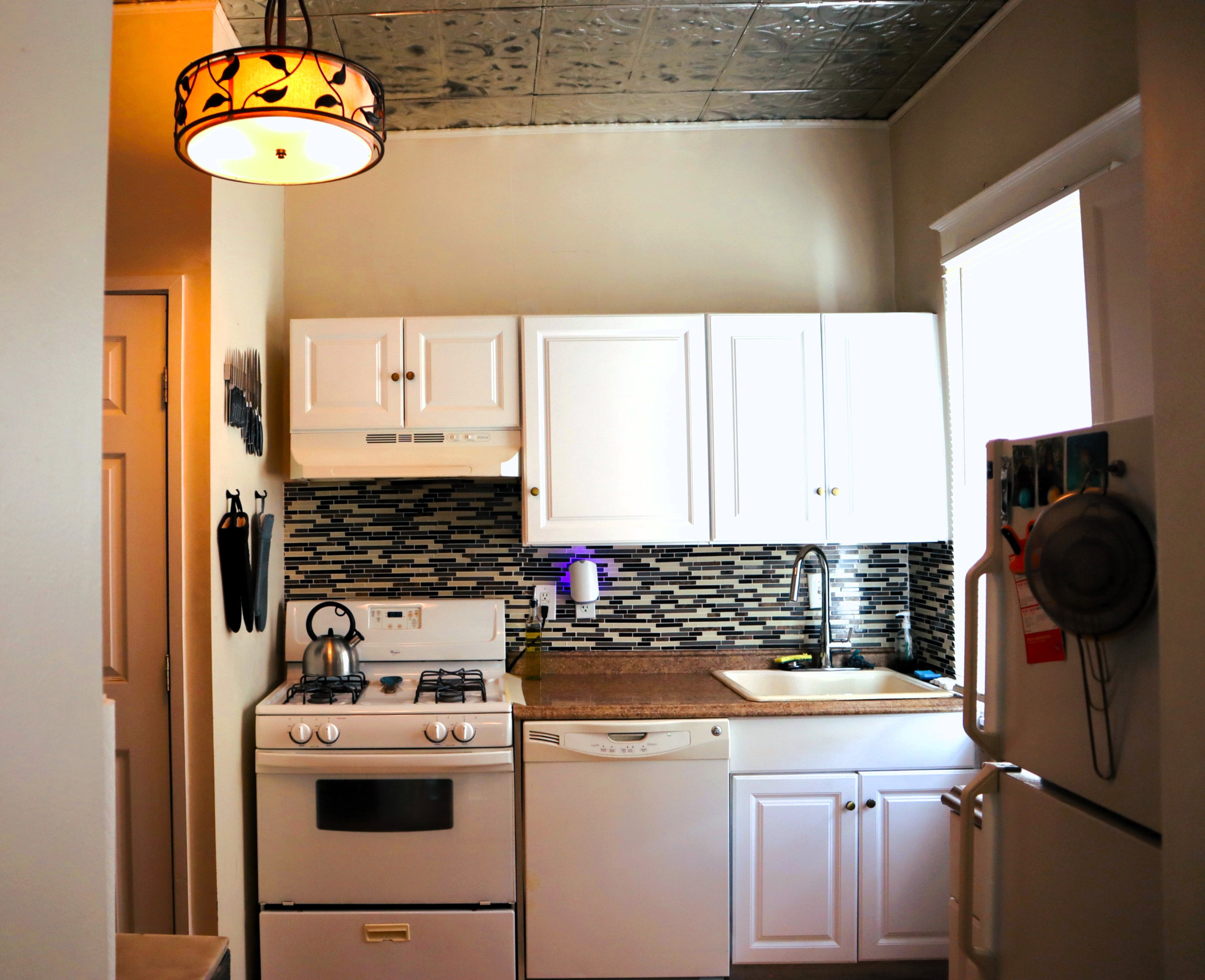 Compact kitchen featuring a pressed tin ceiling, white cabinetry, and a mosaic tile backsplash