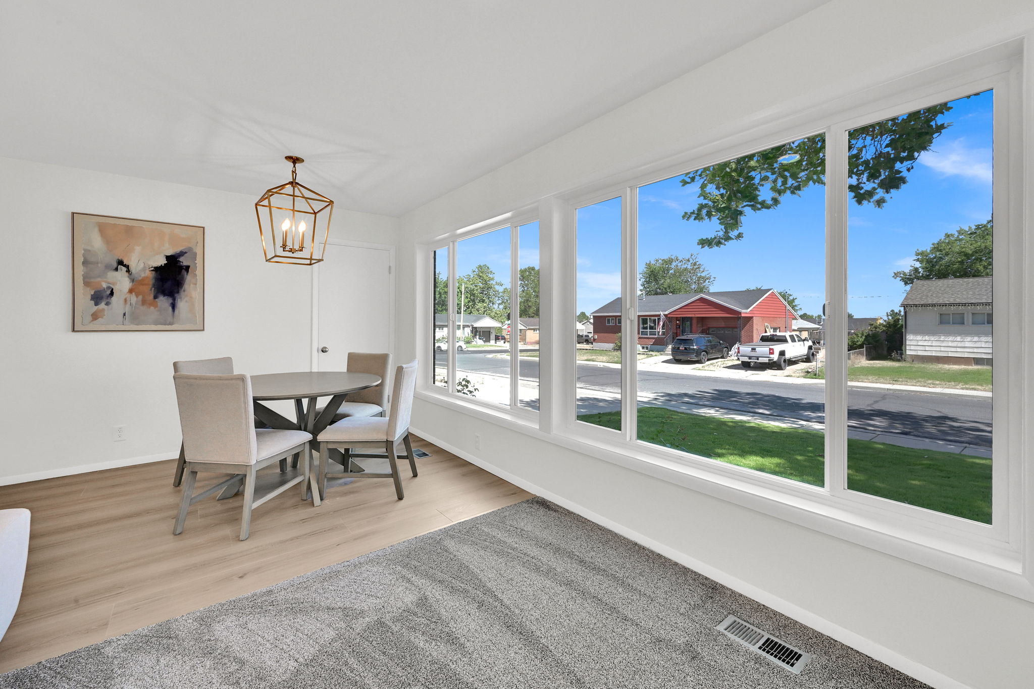 Bright interior with a wall of large windows, light wood-finish flooring, white walls, and a geometric-style pendant light fixture
