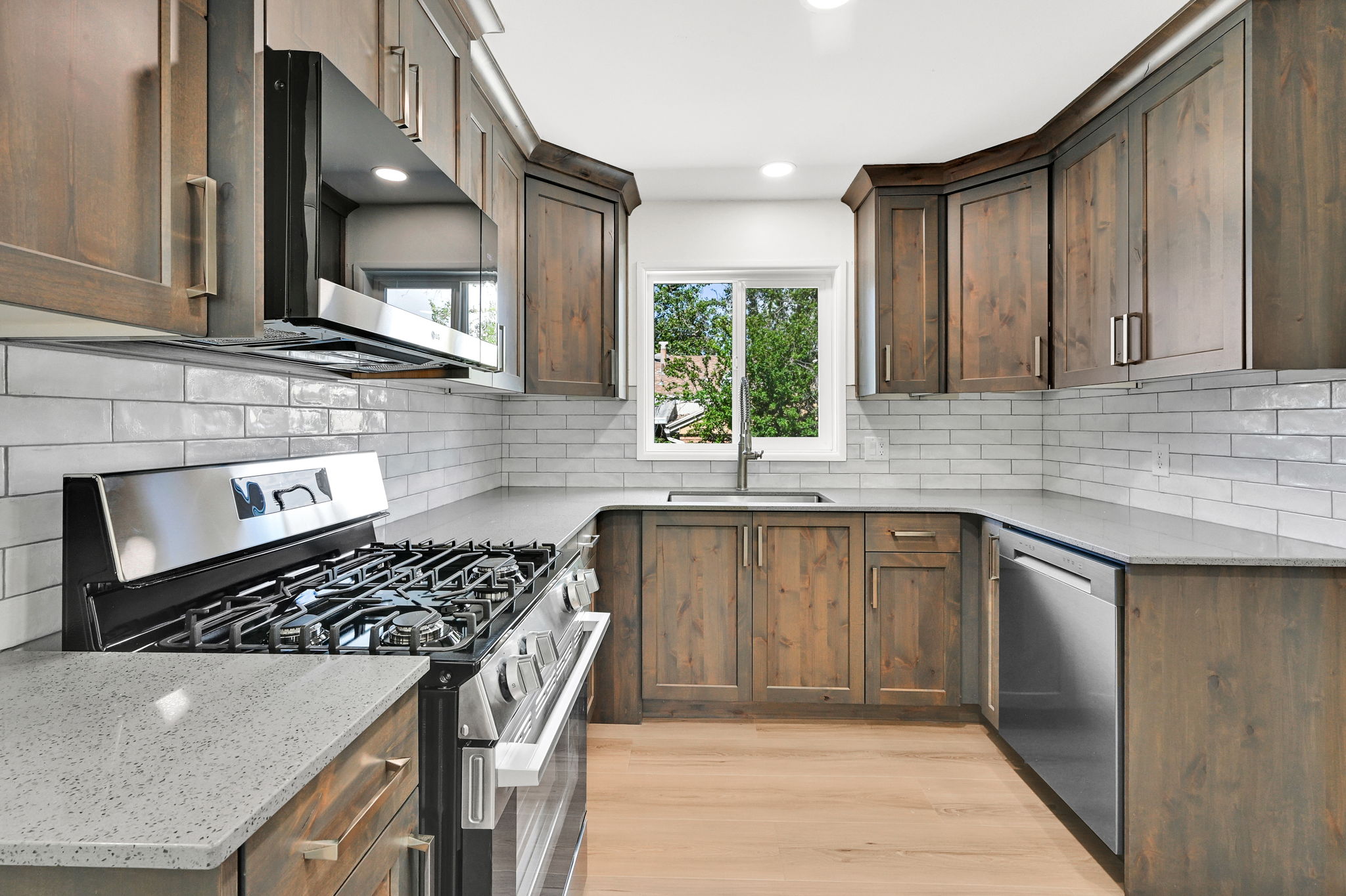 Kitchen featuring wood-finish cabinetry, light-toned countertops, a stainless steel gas range, a stainless steel dishwasher, and a subway tile backsplash