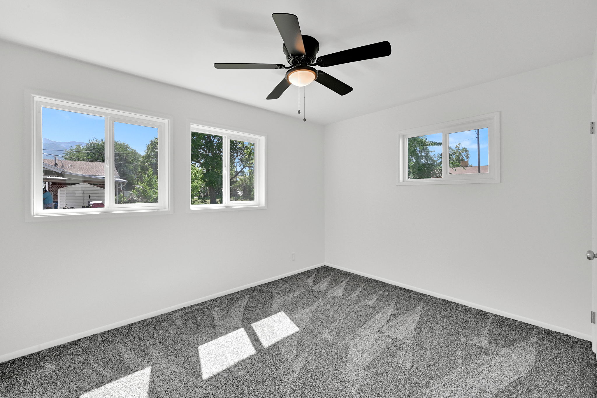 Room featuring gray patterned carpet, white walls, and a black ceiling fan with an integrated light fixture