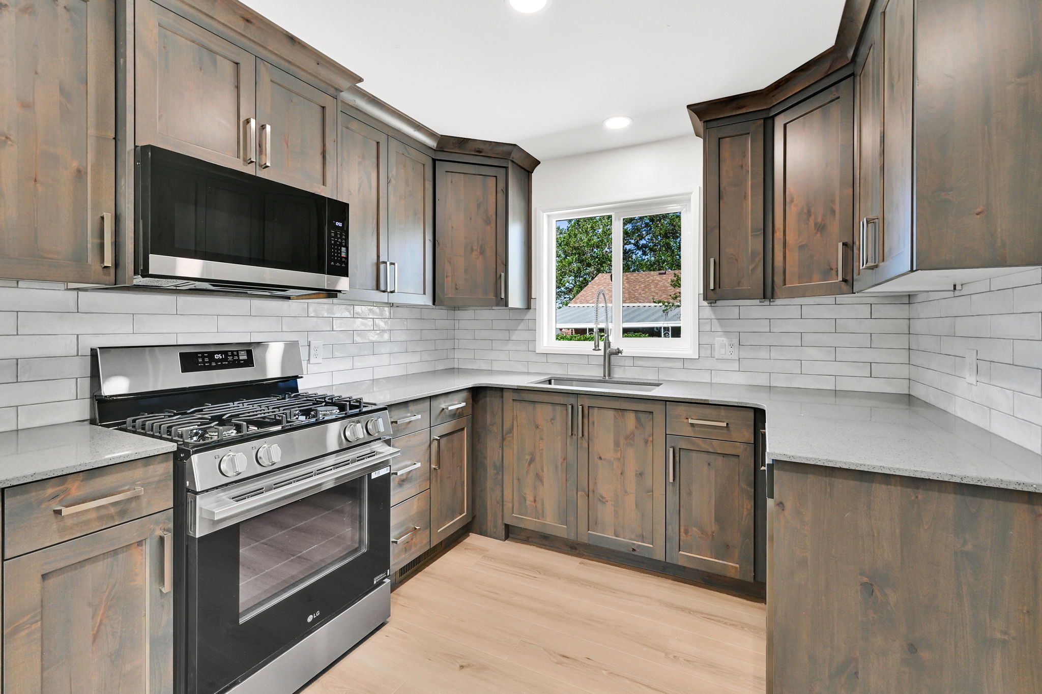 Modern kitchen featuring wood-finish cabinetry, stainless steel appliances, a white subway tile backsplash, light-colored countertops, and wood-finish flooring