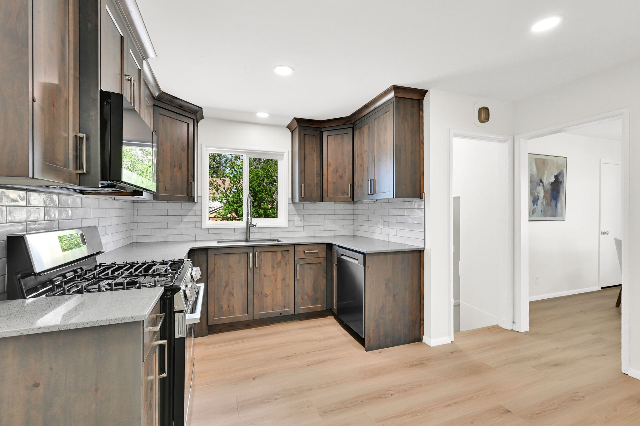 Kitchen featuring dark wood-finish cabinetry, light-toned countertops, a full subway tile backsplash, stainless steel appliances, and light wood-finish flooring