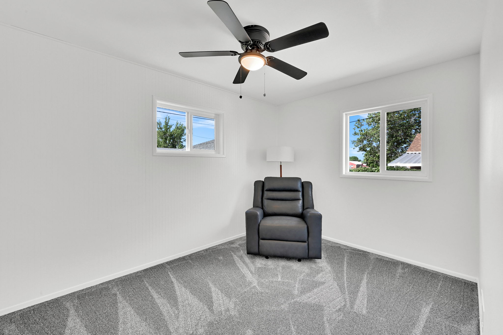 Bright room featuring a black ceiling fan with integrated lighting, two windows with white trim, and light gray patterned carpet