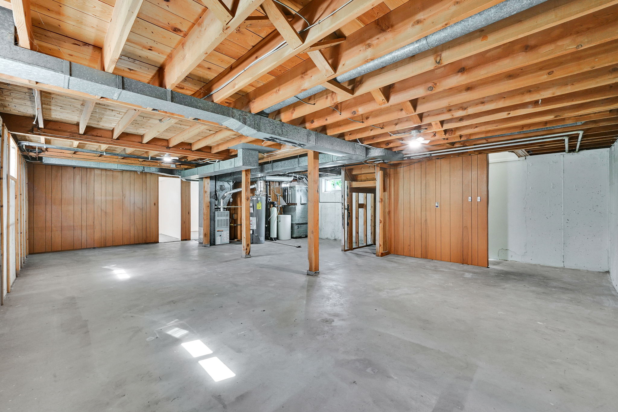 Unfinished basement offering exposed wood ceiling joists, concrete flooring, and wood-paneled walls