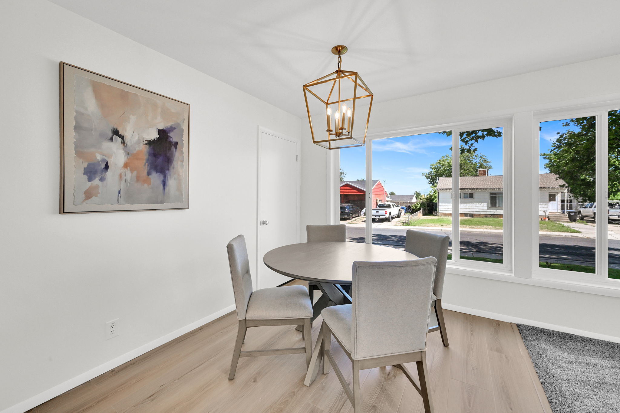 Bright dining area featuring wood-finish flooring, a contemporary geometric chandelier, and multiple large windows