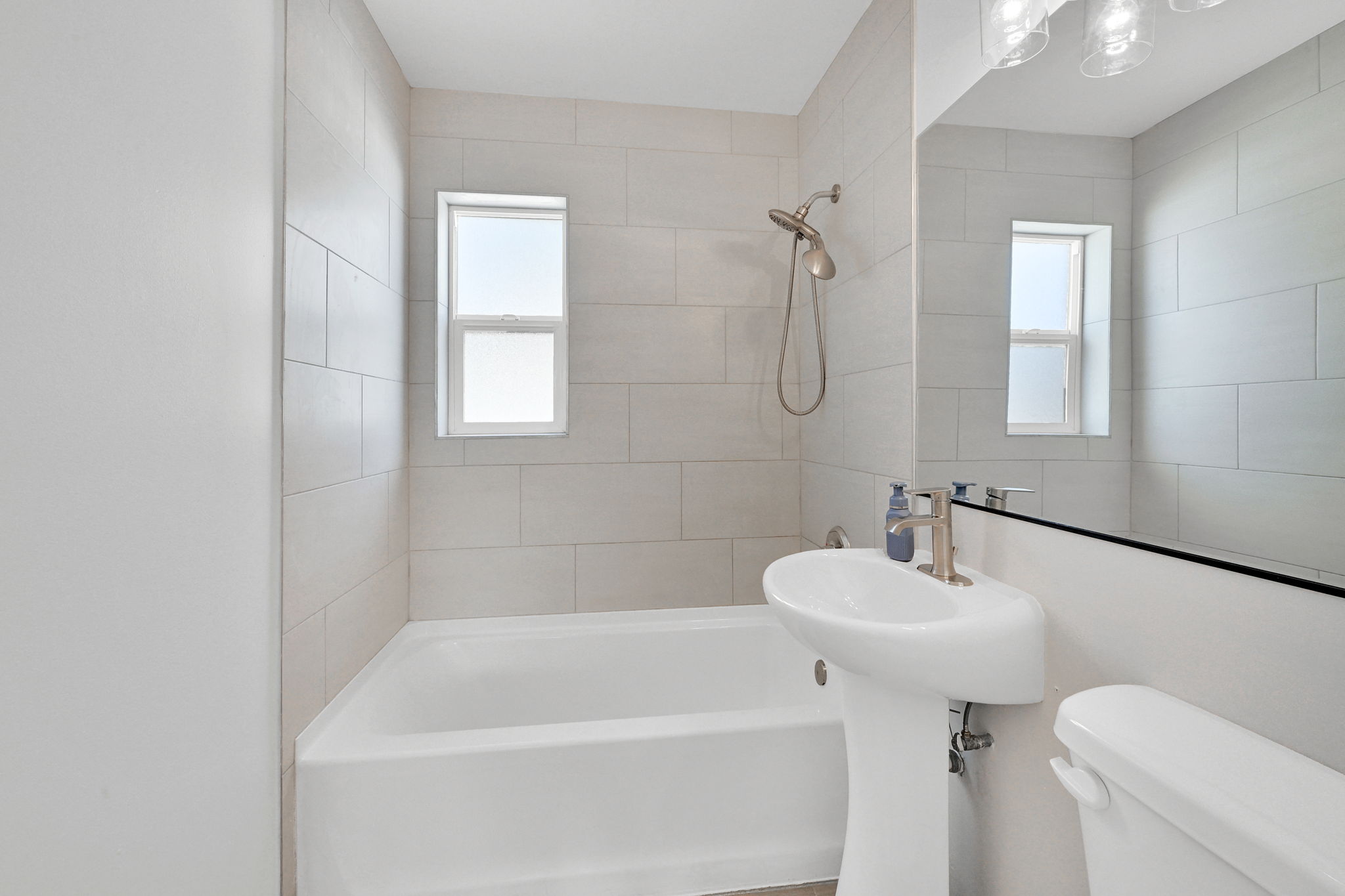 Bathroom featuring a pedestal sink, brushed nickel faucet, full-height wall tiling, and a bathtub with an integrated shower head