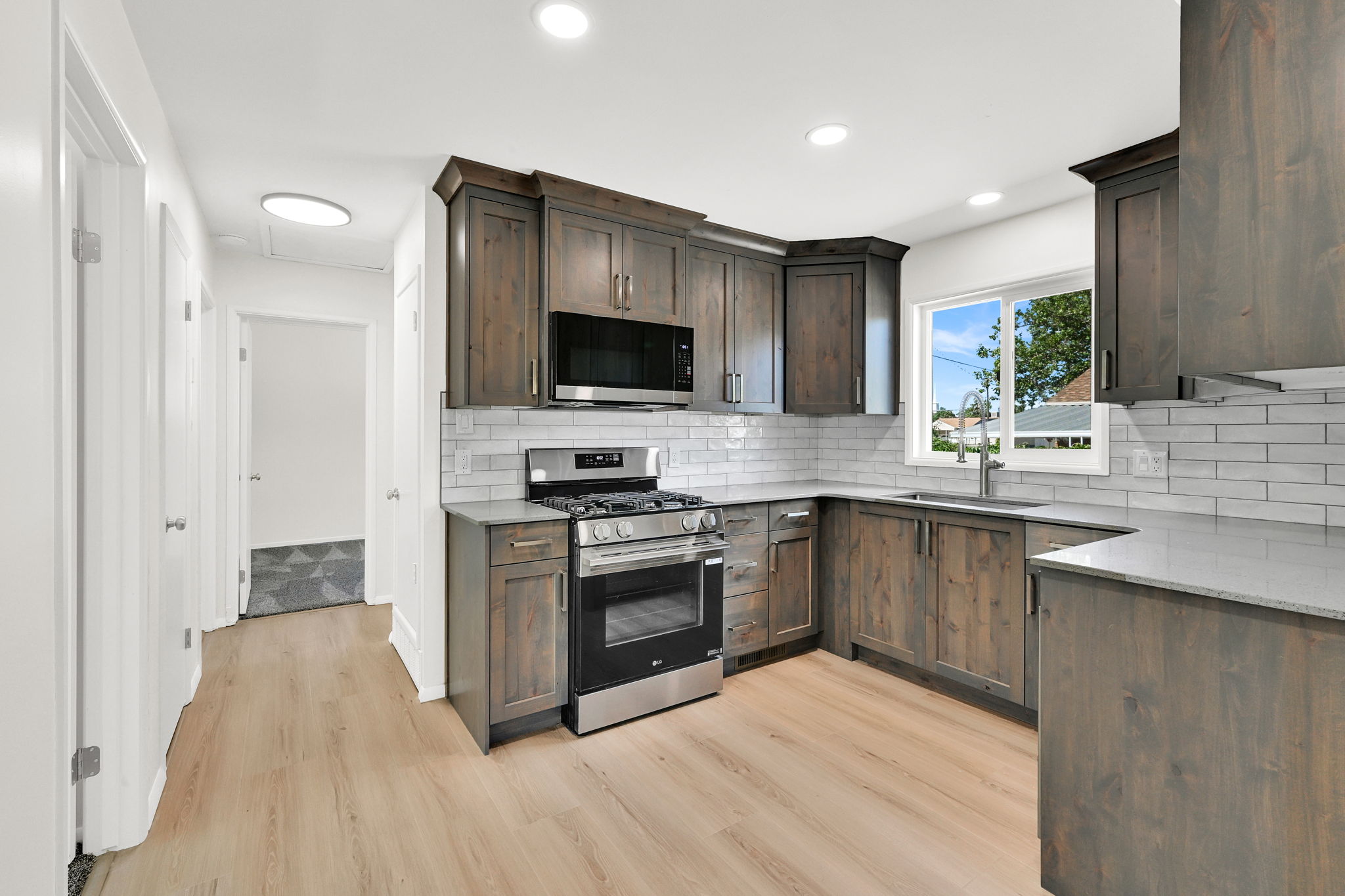 Modern kitchen featuring wood-finish cabinetry, stainless steel appliances, light countertops, subway tile backsplash, and recessed lighting