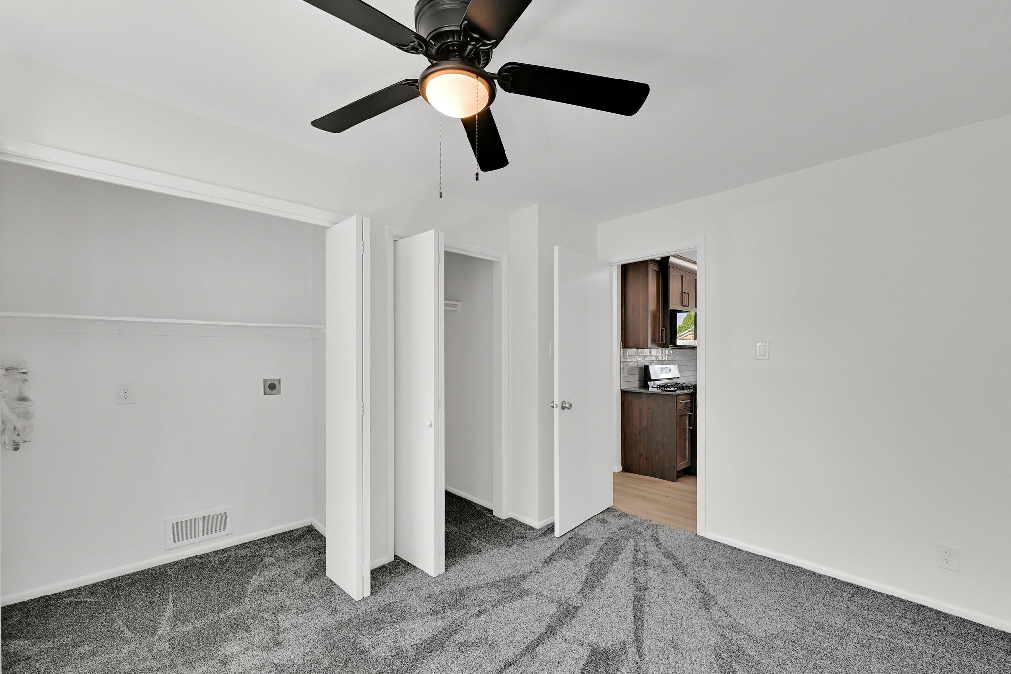 Bedroom with dark gray carpeting, a black ceiling fan with an integrated light fixture, a closet with bi-fold doors, and a laundry area featuring hookups and upper shelving
