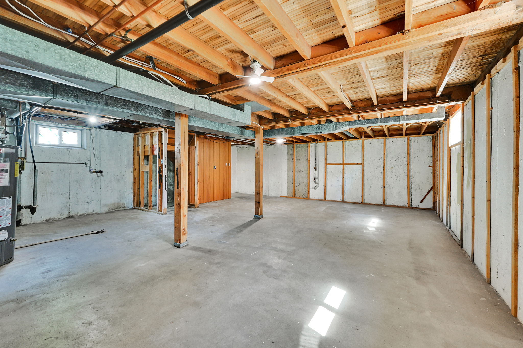 Expansive unfinished basement featuring a concrete floor, exposed wood ceiling joists, and exposed concrete walls