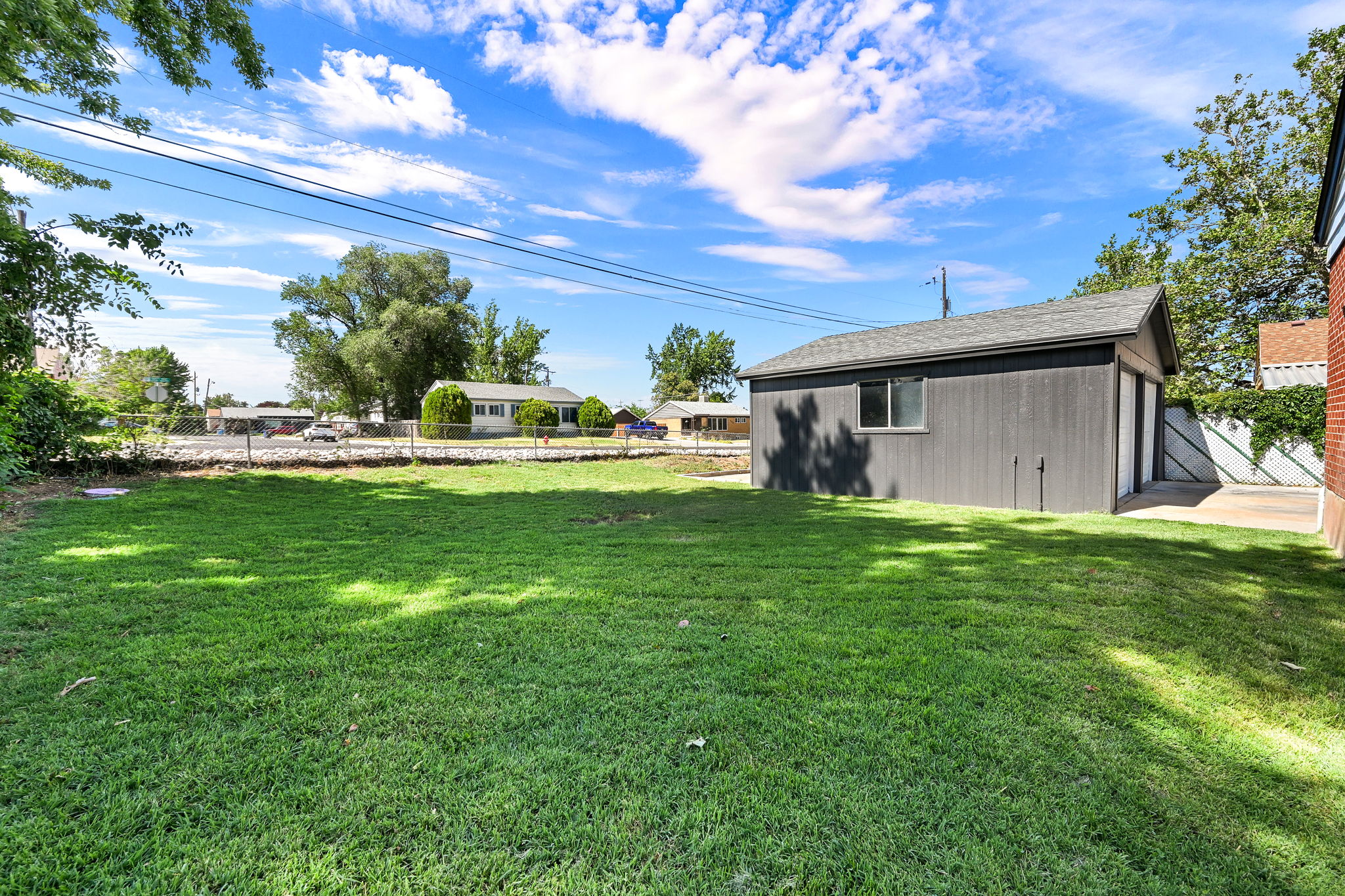 Expansive green lawn with a detached auxiliary building featuring gray siding and a shingle roof