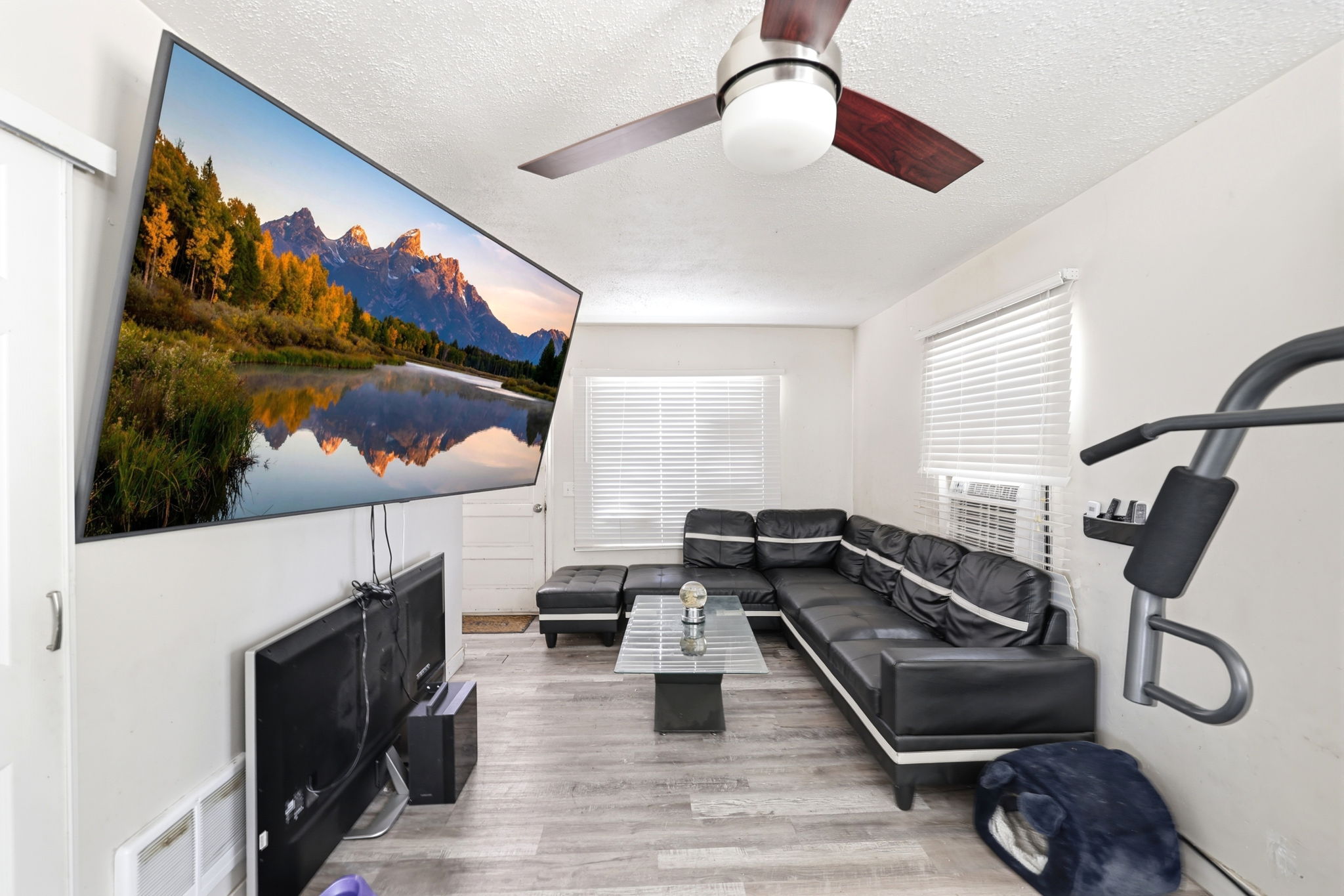 Living area featuring wood-finish flooring, white walls, and a ceiling fan with integrated lighting