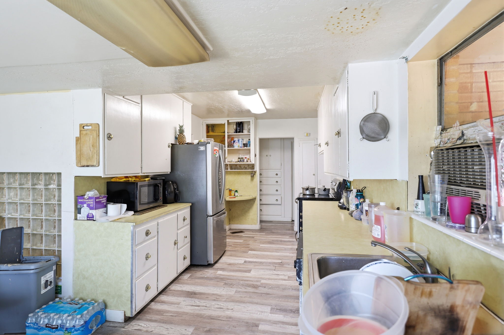 Spacious kitchen featuring wood-finish flooring, white cabinetry, a stainless steel refrigerator, a built-in sink, and a glass block partition