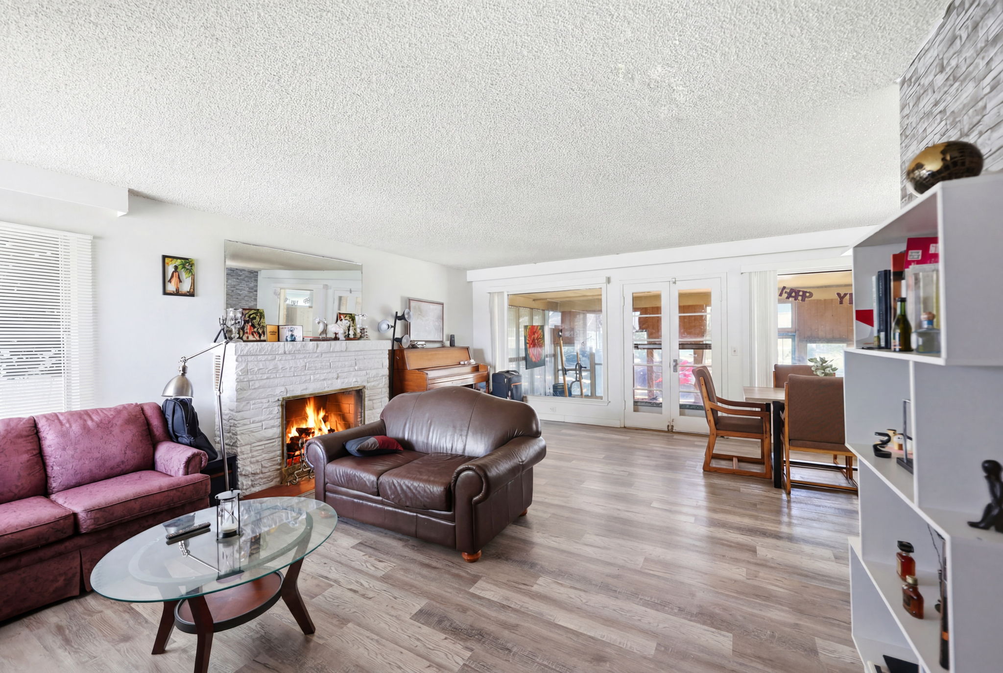 Spacious living area featuring wood-finish flooring, a white brick-clad fireplace, and multiple windows