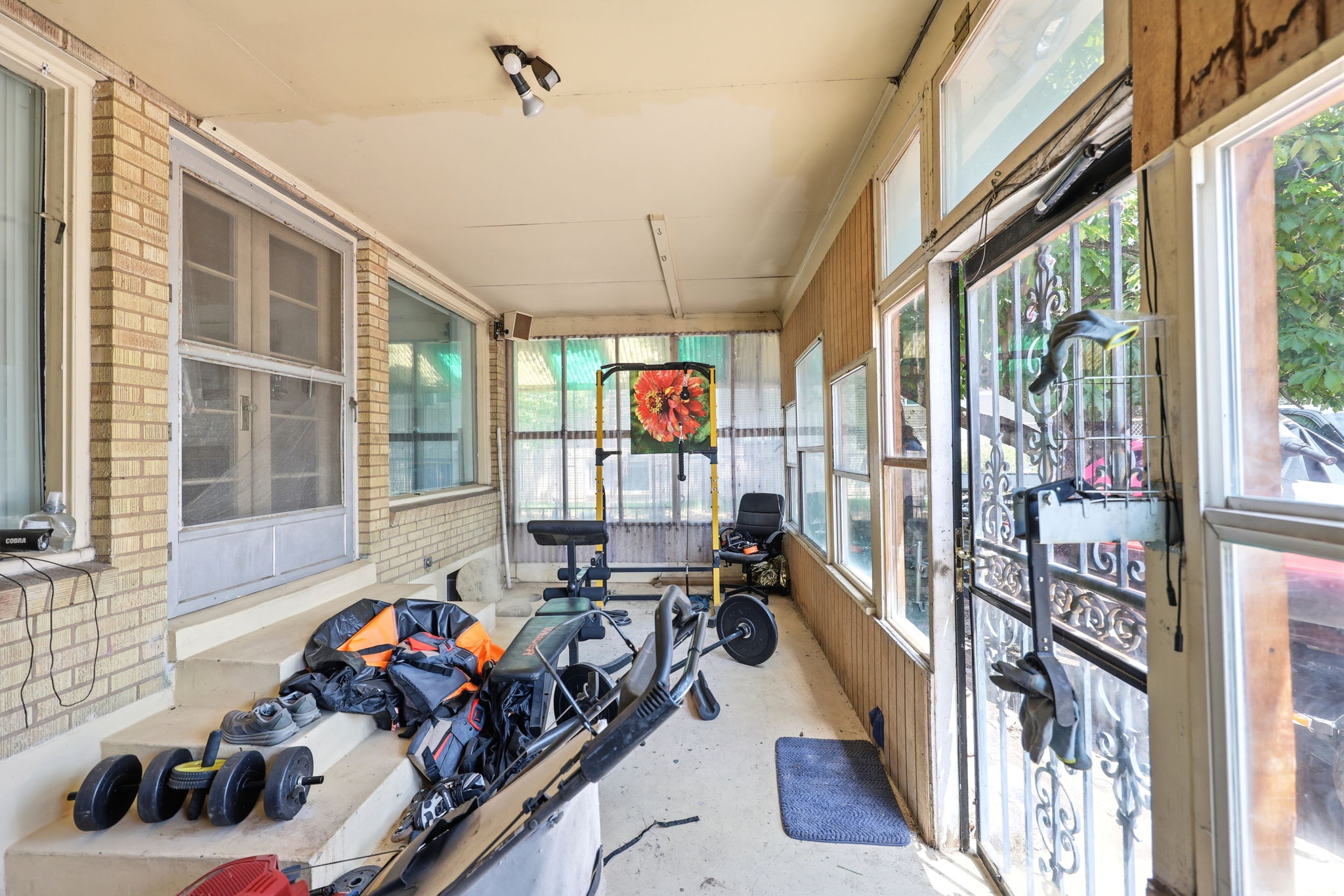Enclosed porch featuring a brick exterior wall, multiple windows, a screened entry door, and a security door with ornate metalwork