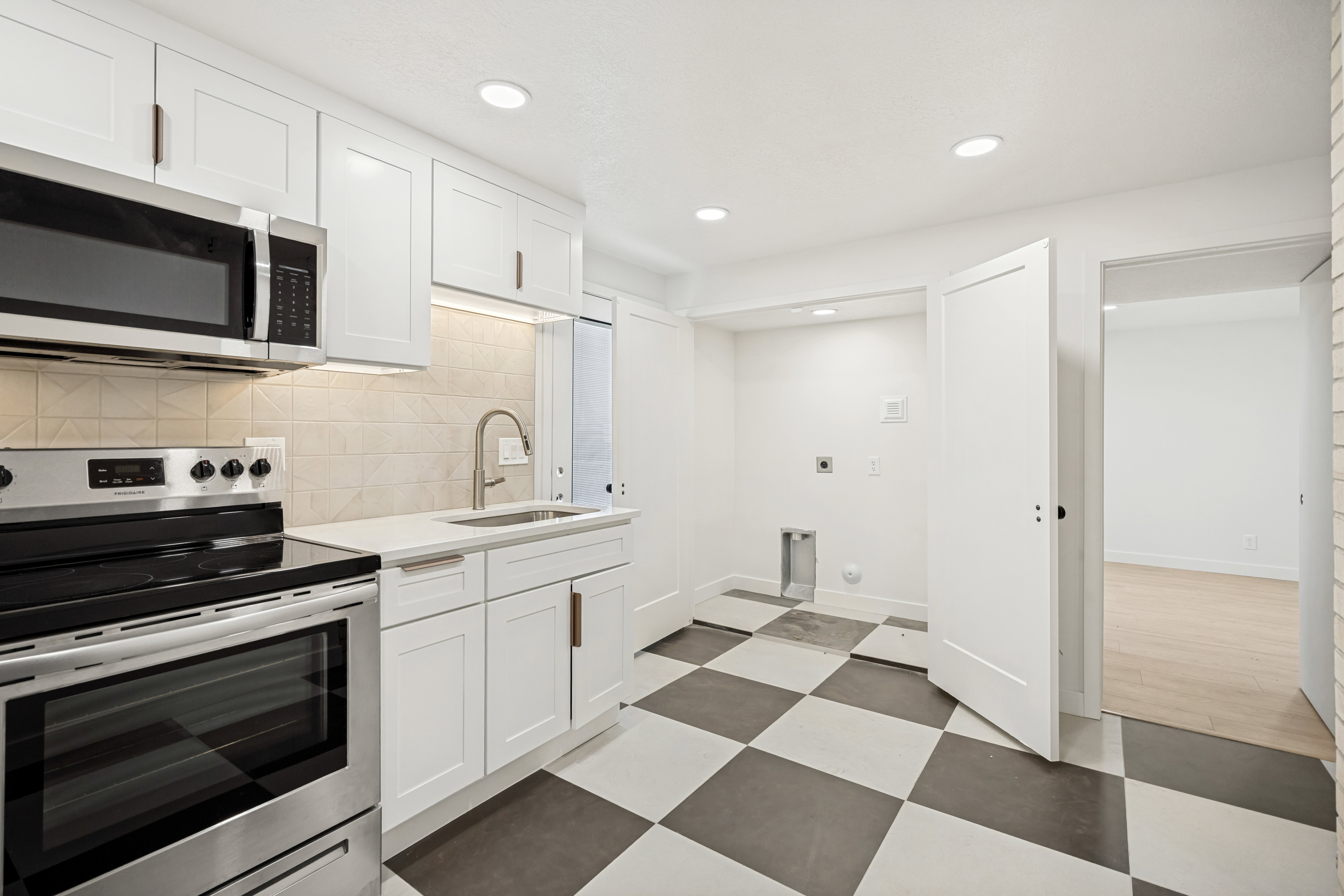 Kitchenette featuring stainless steel appliances, white cabinetry with bronze hardware, a light-toned tile backsplash, and a checkered floor