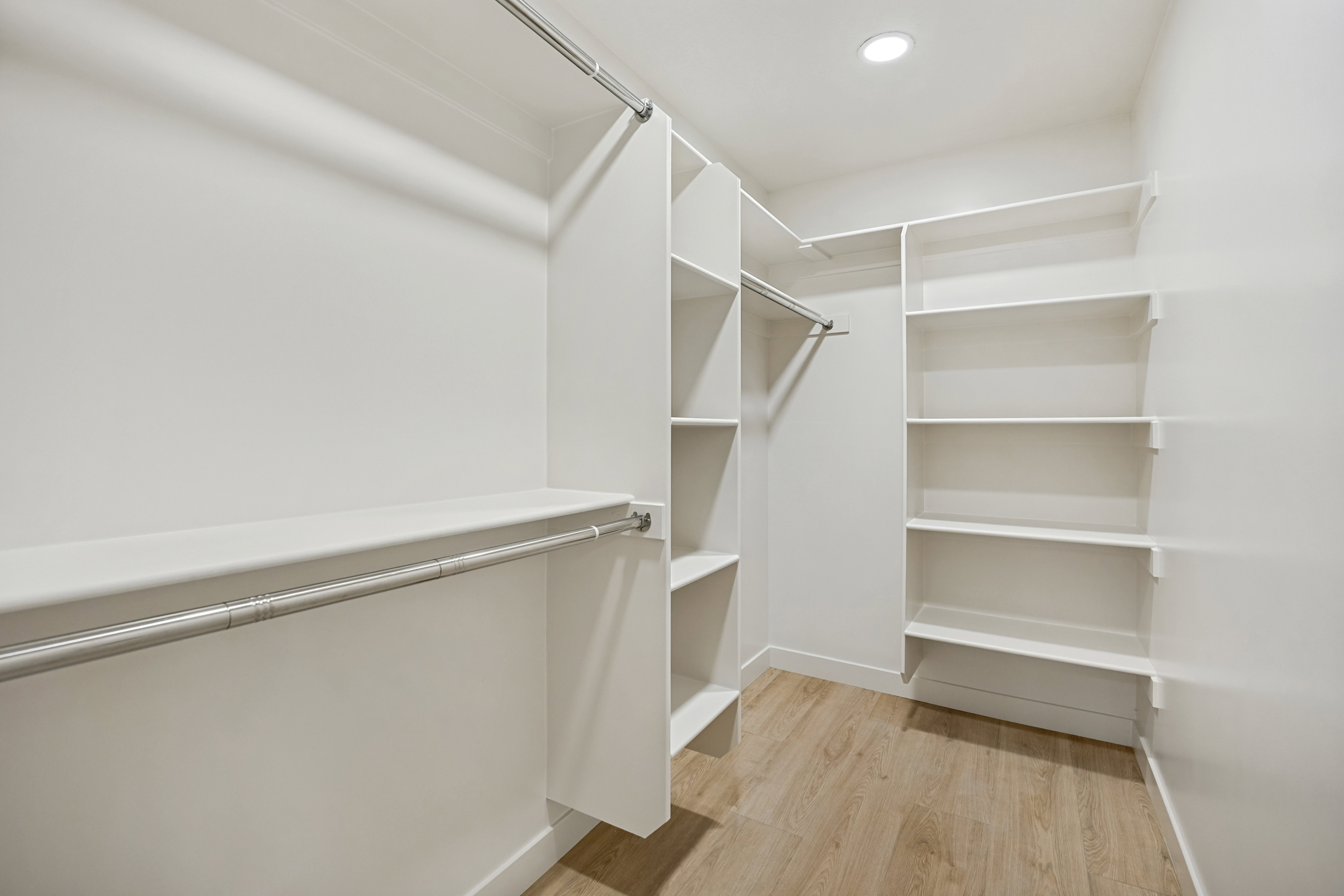 Walk-in closet featuring light wood-finish flooring, recessed lighting, white built-in shelving, and multiple clothing rods
