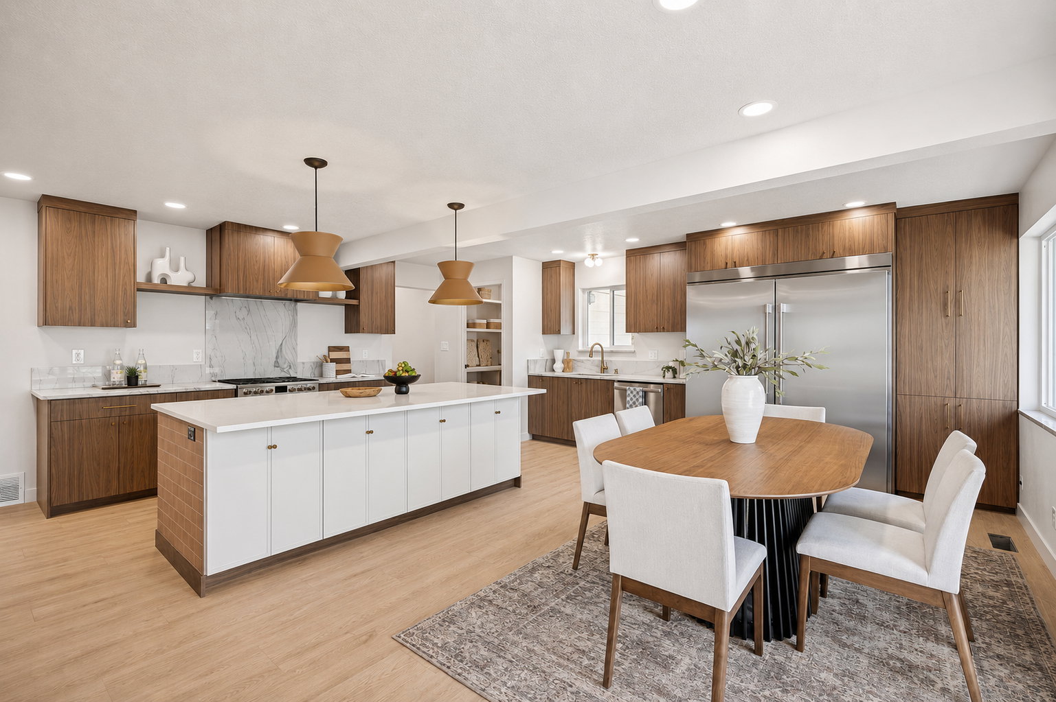 Open-concept kitchen featuring wood-finish cabinetry, a large center island with a light-toned countertop, stainless steel appliances, a range with a marble-patterned backsplash, and recessed lighting