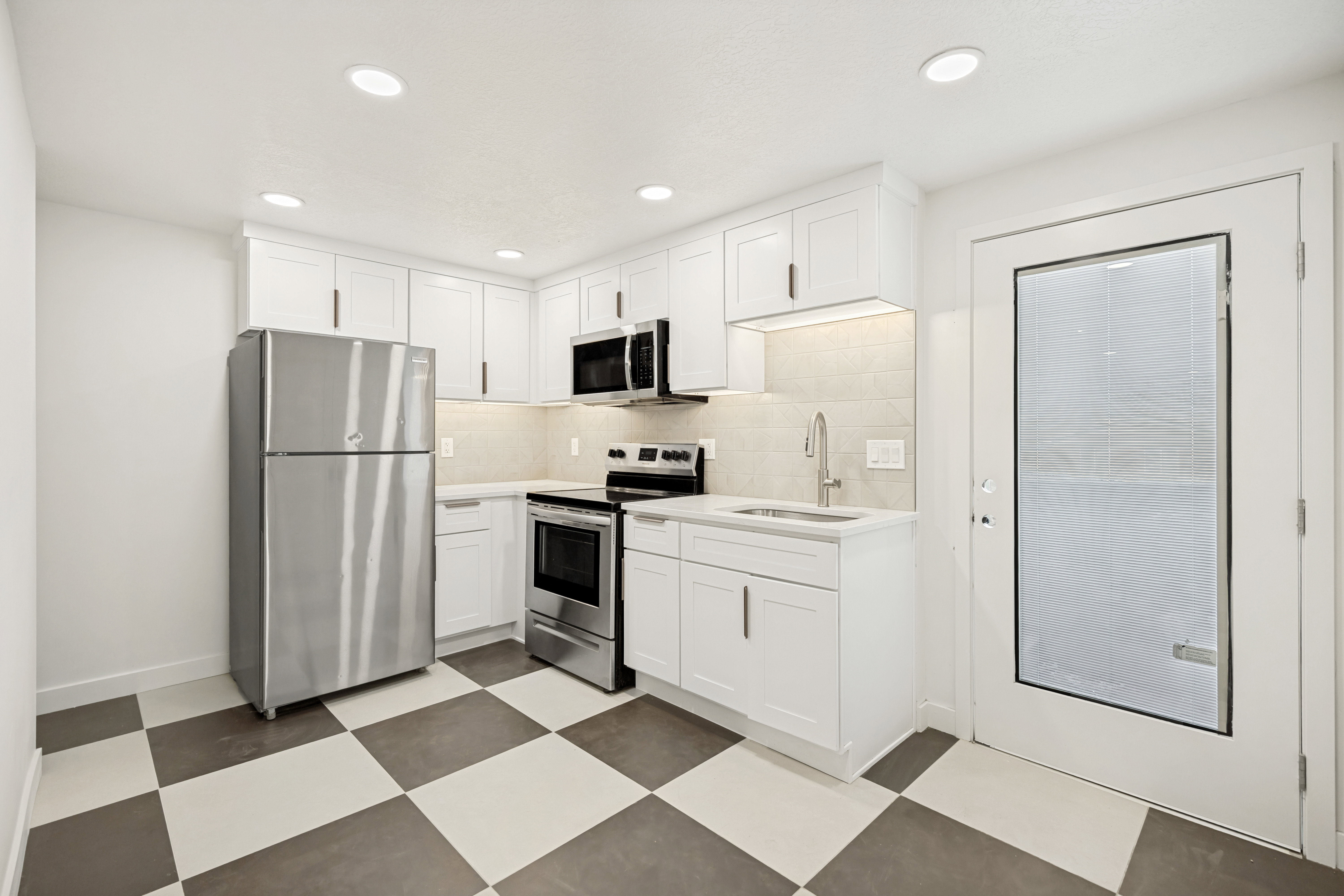 Modern kitchen featuring white shaker cabinetry, stainless steel appliances, a checkerboard tile floor, and recessed lighting