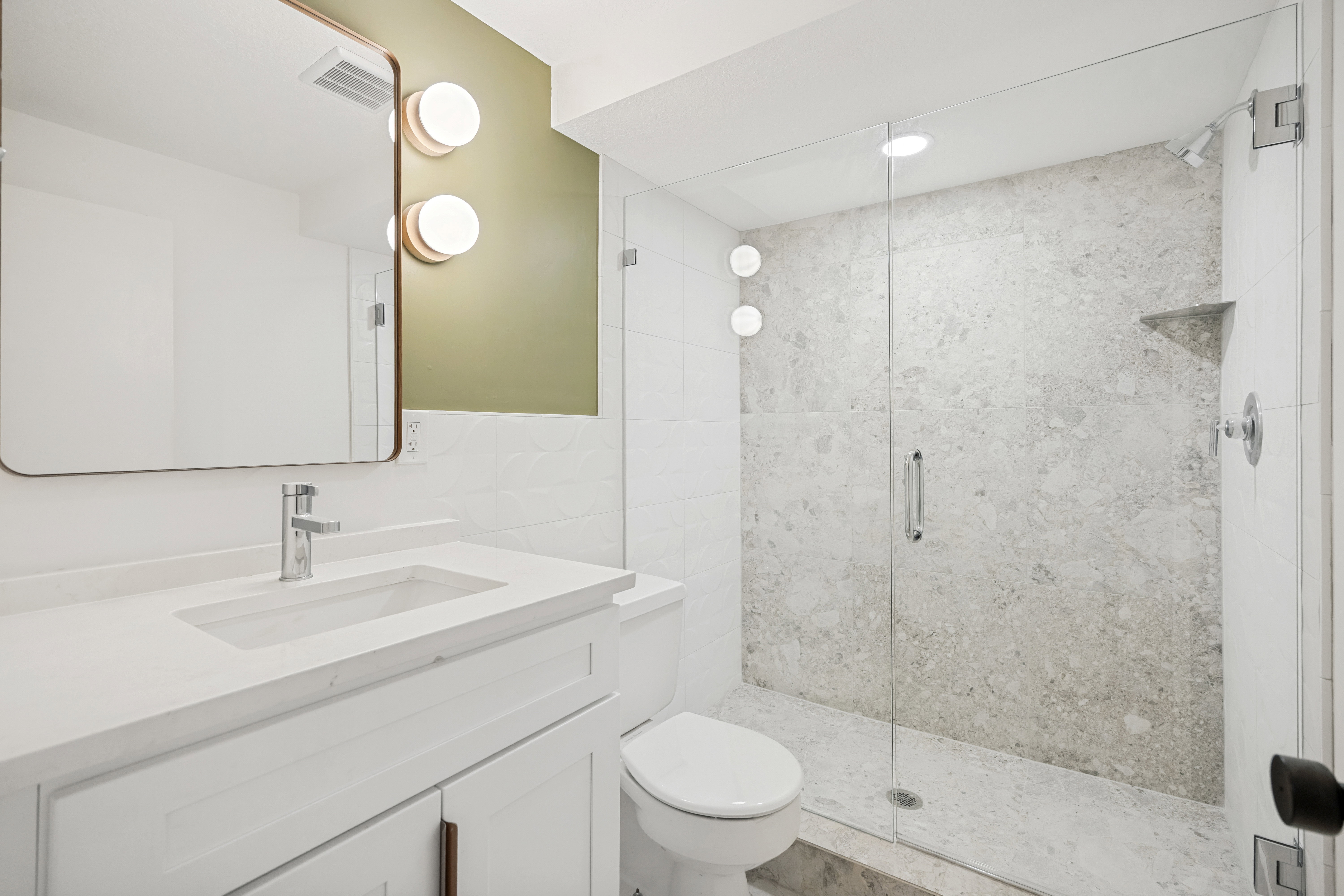 Full bathroom featuring a frameless glass shower enclosure, a built-in shower niche, a white vanity with an integrated sink, a contemporary chrome faucet, and a rectangular wall mirror with rounded corners