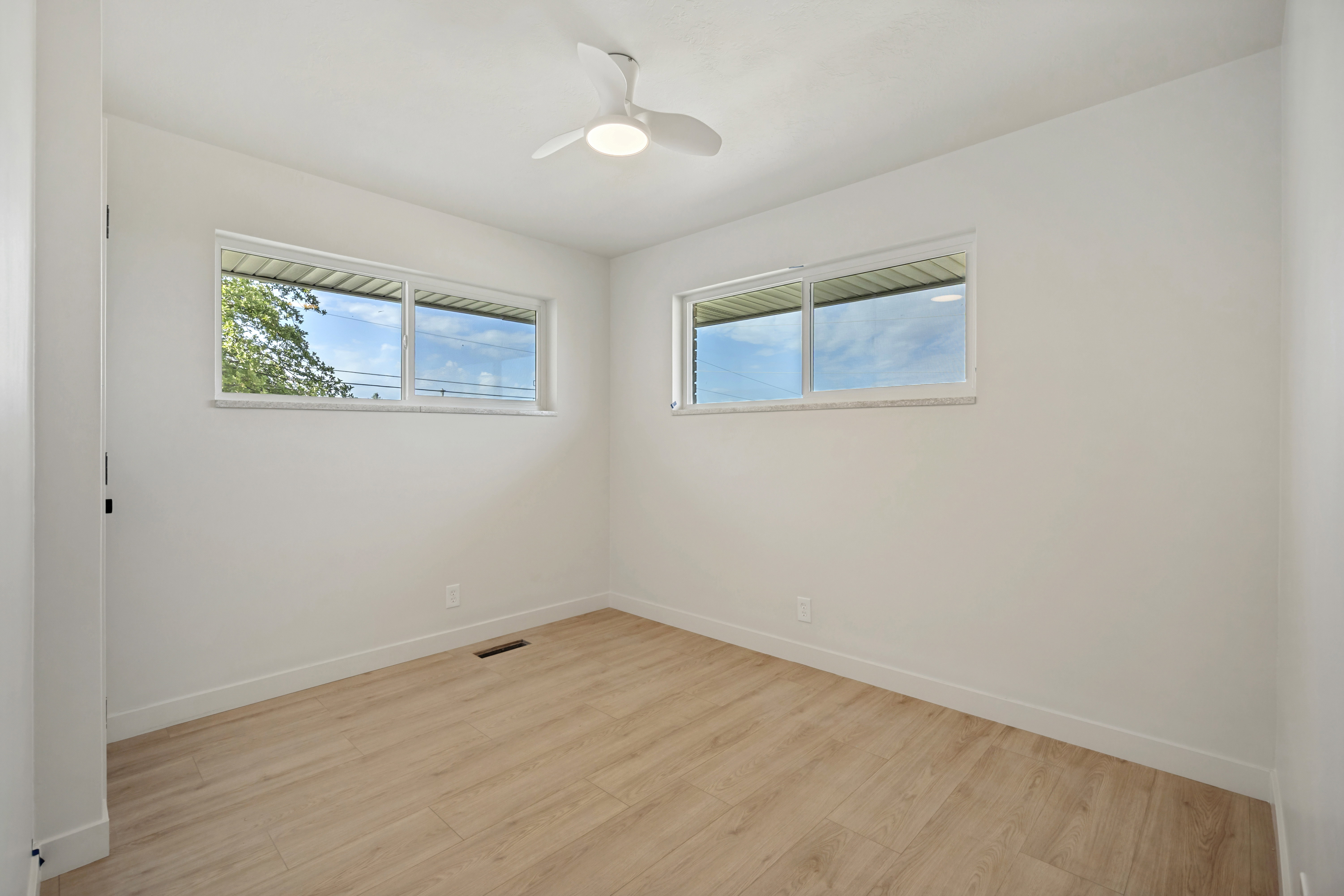 Bright interior space featuring wood-finish flooring, white walls, and a contemporary ceiling fan with integrated lighting