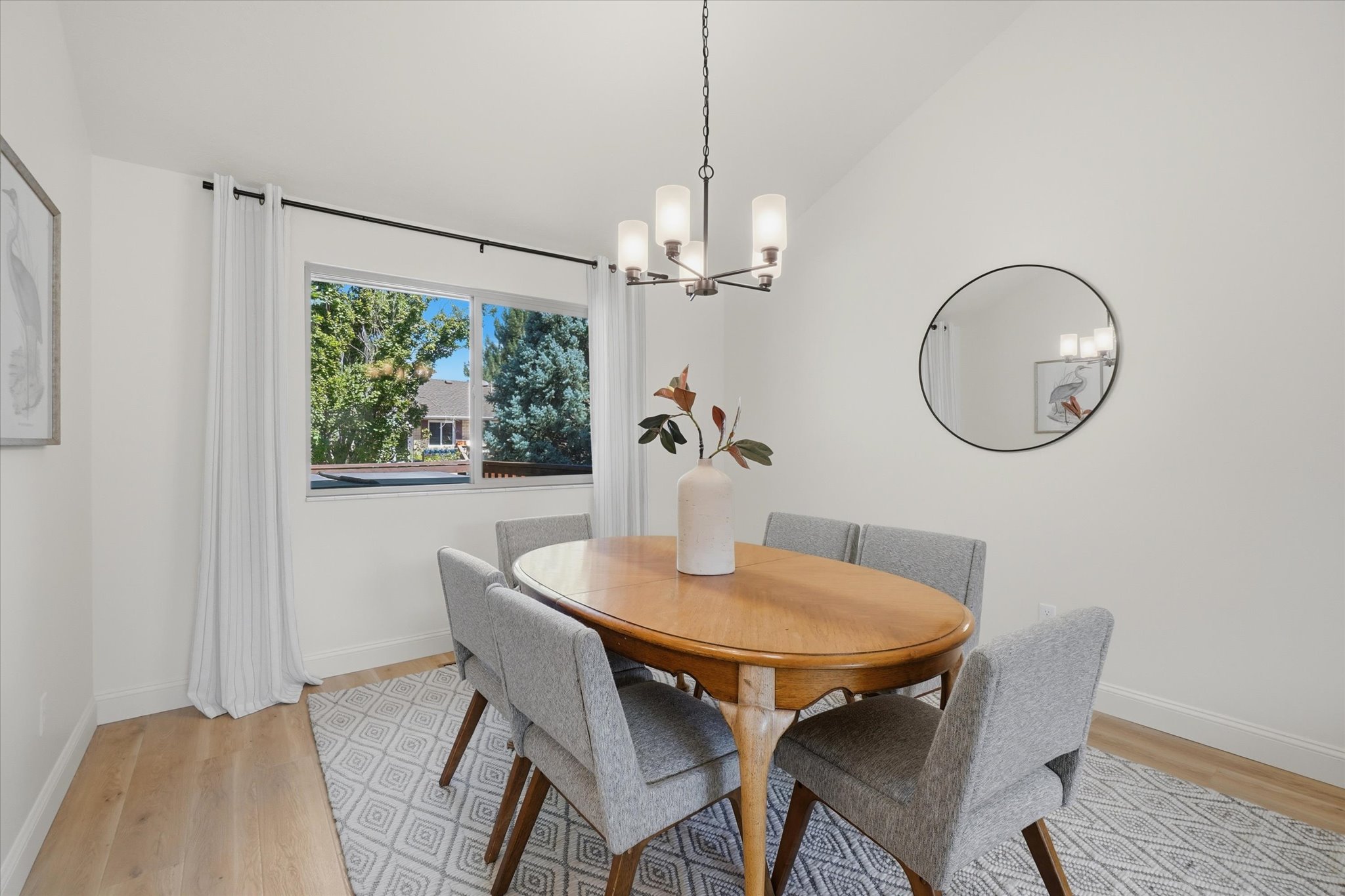 Dining area featuring light wood-finish flooring, a contemporary chandelier, a window with exterior views, and a round wall mirror