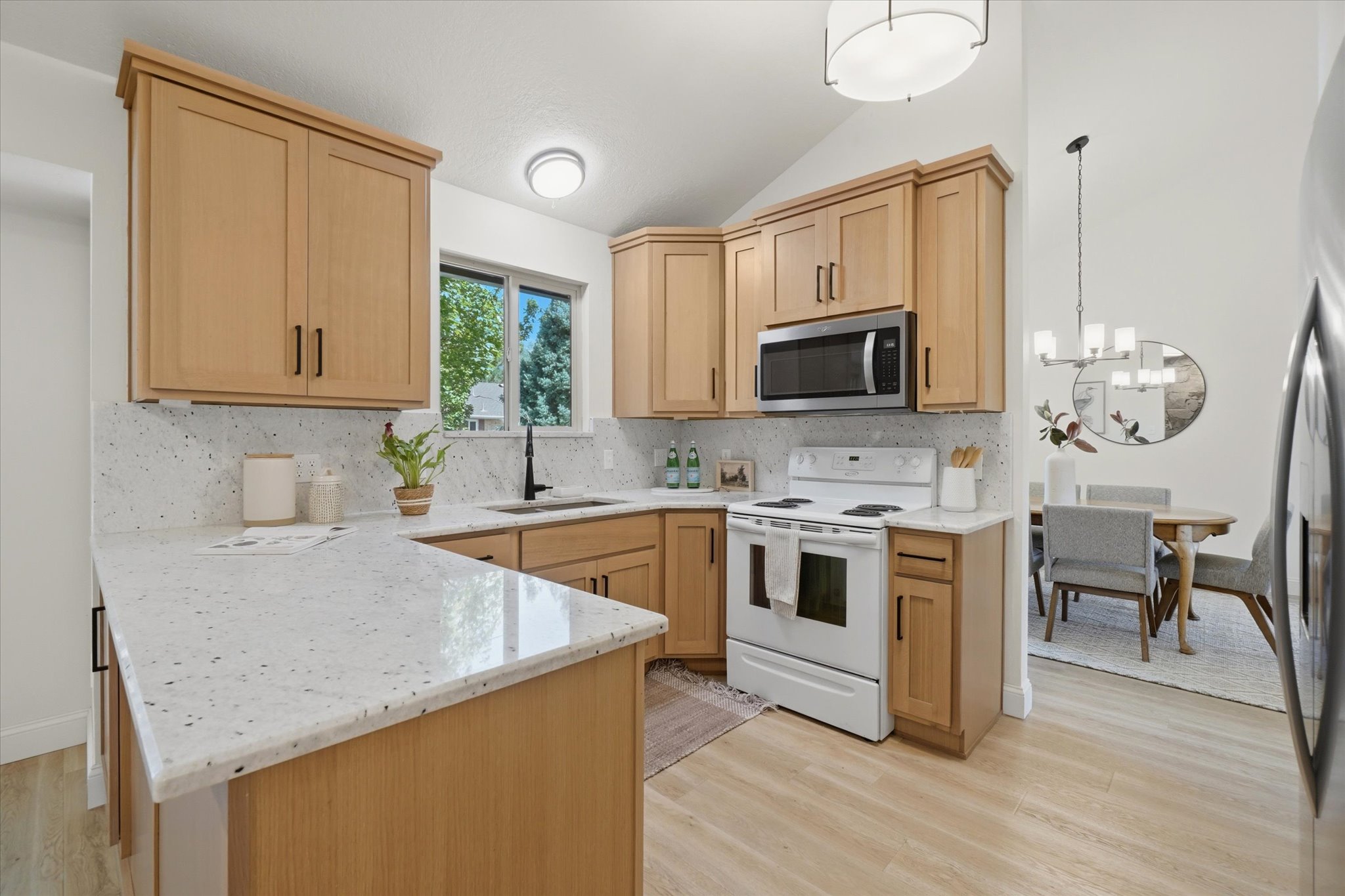 Kitchen featuring light wood cabinetry, white speckled countertops, and a white tile backsplash