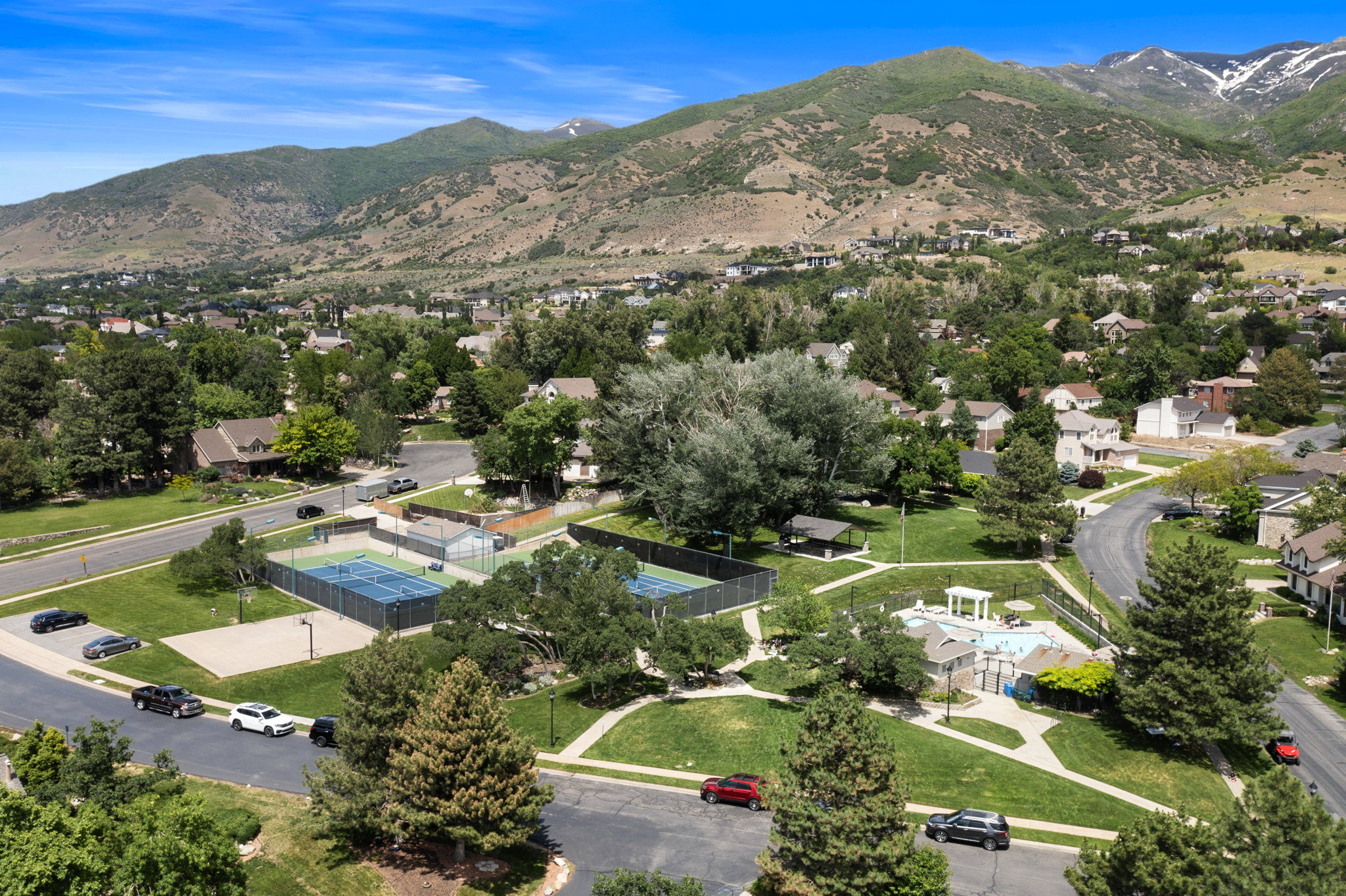 Mountain backdrop framing a residential community featuring tennis courts, a swimming pool, open green spaces, and mature landscaping