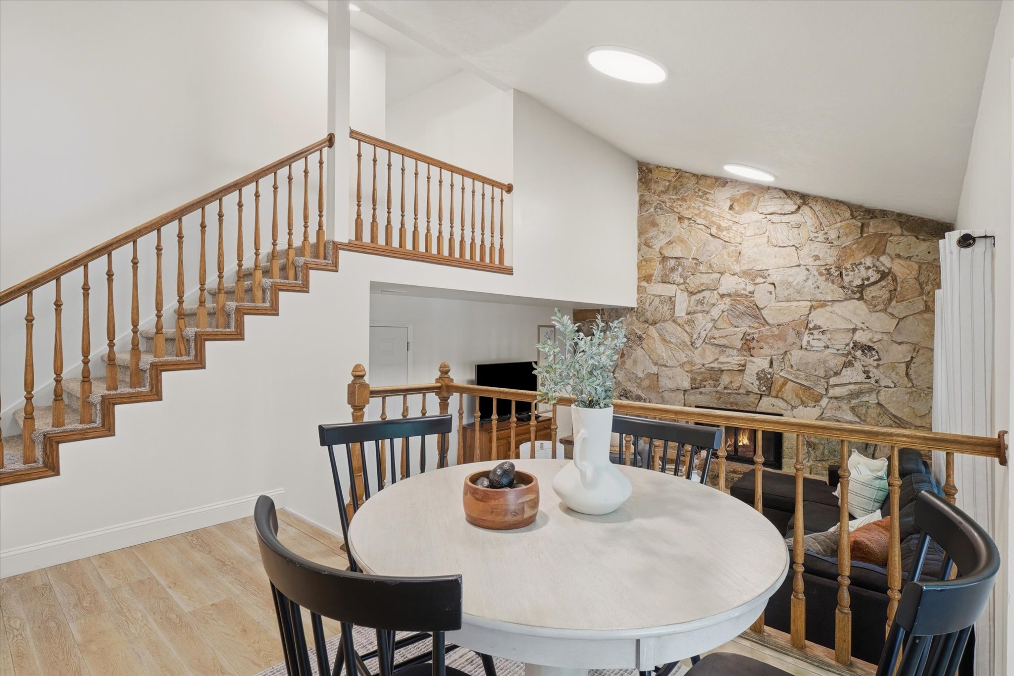 Open-concept interior featuring a stone accent wall with a linear fireplace, vaulted ceilings with skylights, and light wood-finish flooring