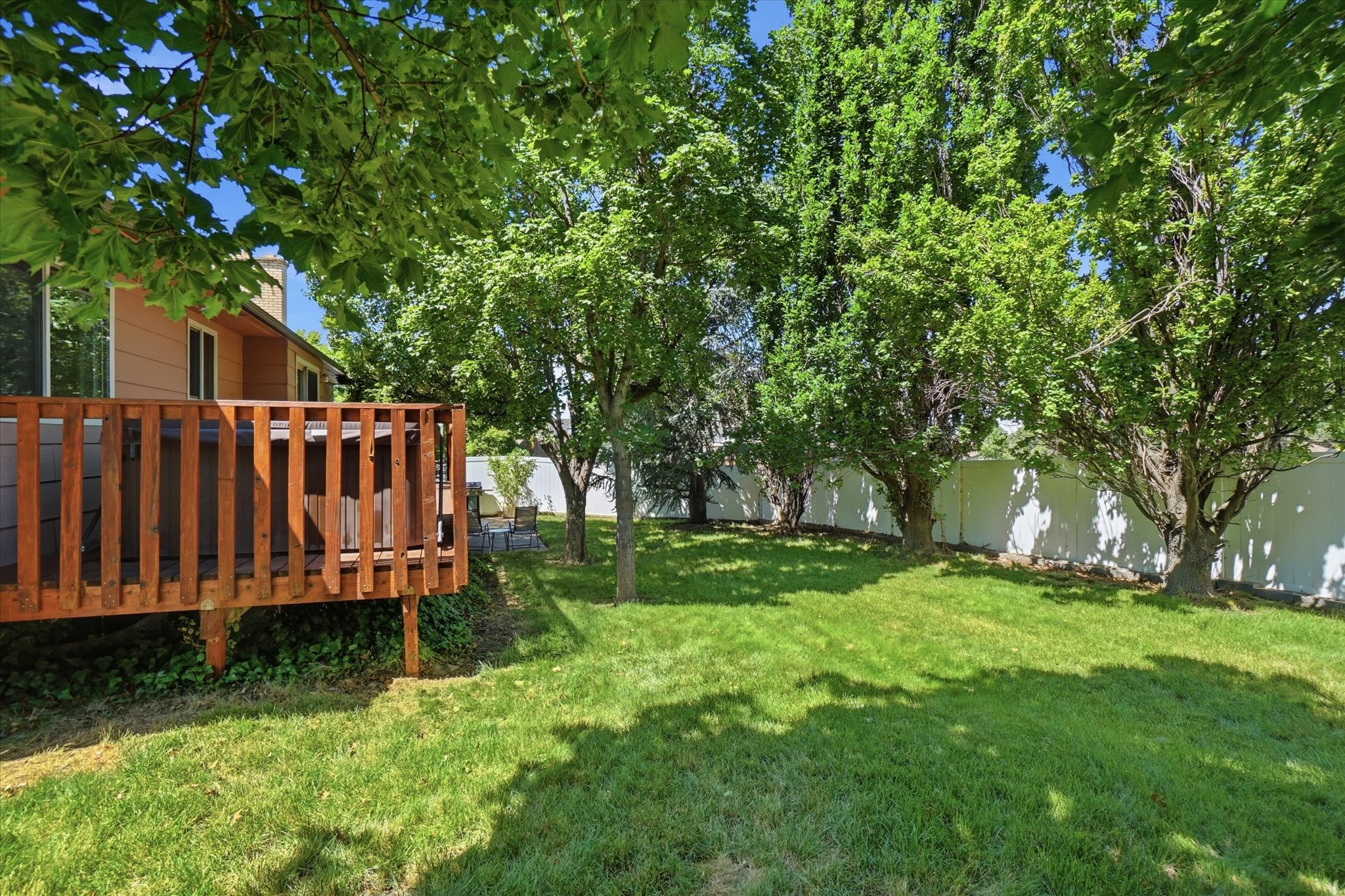 Expansive backyard featuring a manicured lawn, mature trees, and a wooden deck with railing