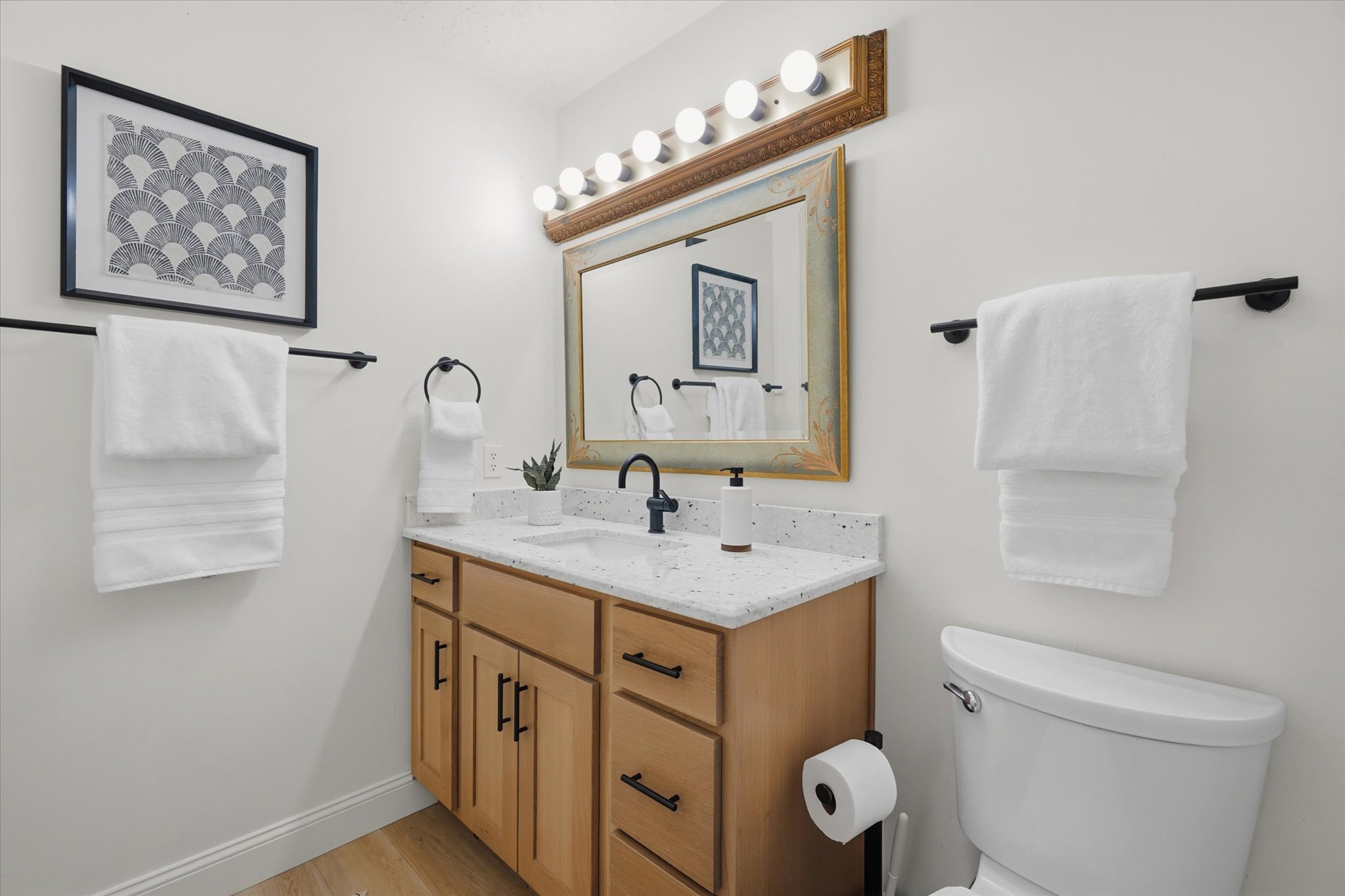 Single vanity with light wood-finish cabinetry, a white countertop featuring an integrated sink, and a matte black faucet