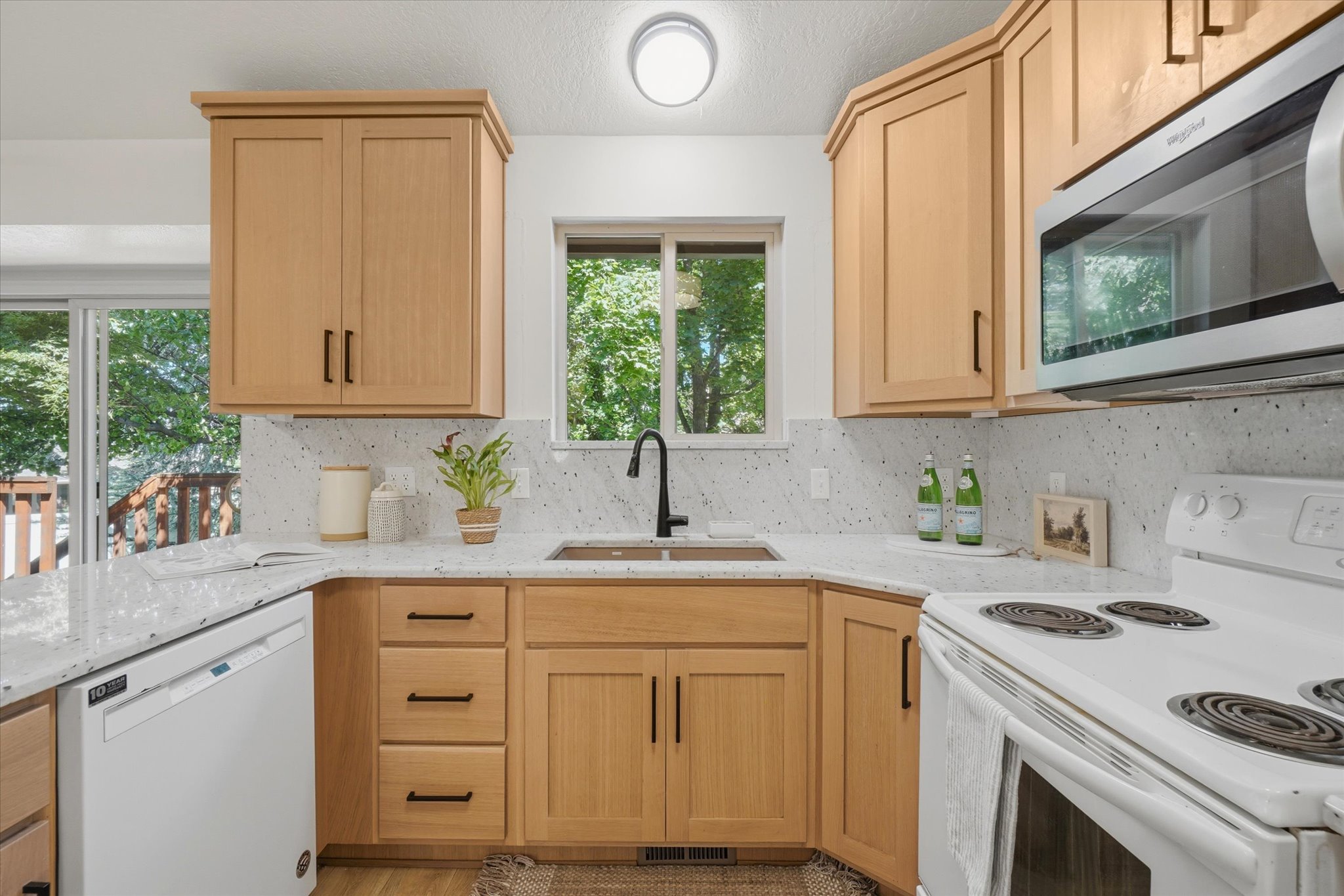 Kitchen featuring light wood cabinetry with dark hardware, a corner sink with a black faucet, and white speckled countertops