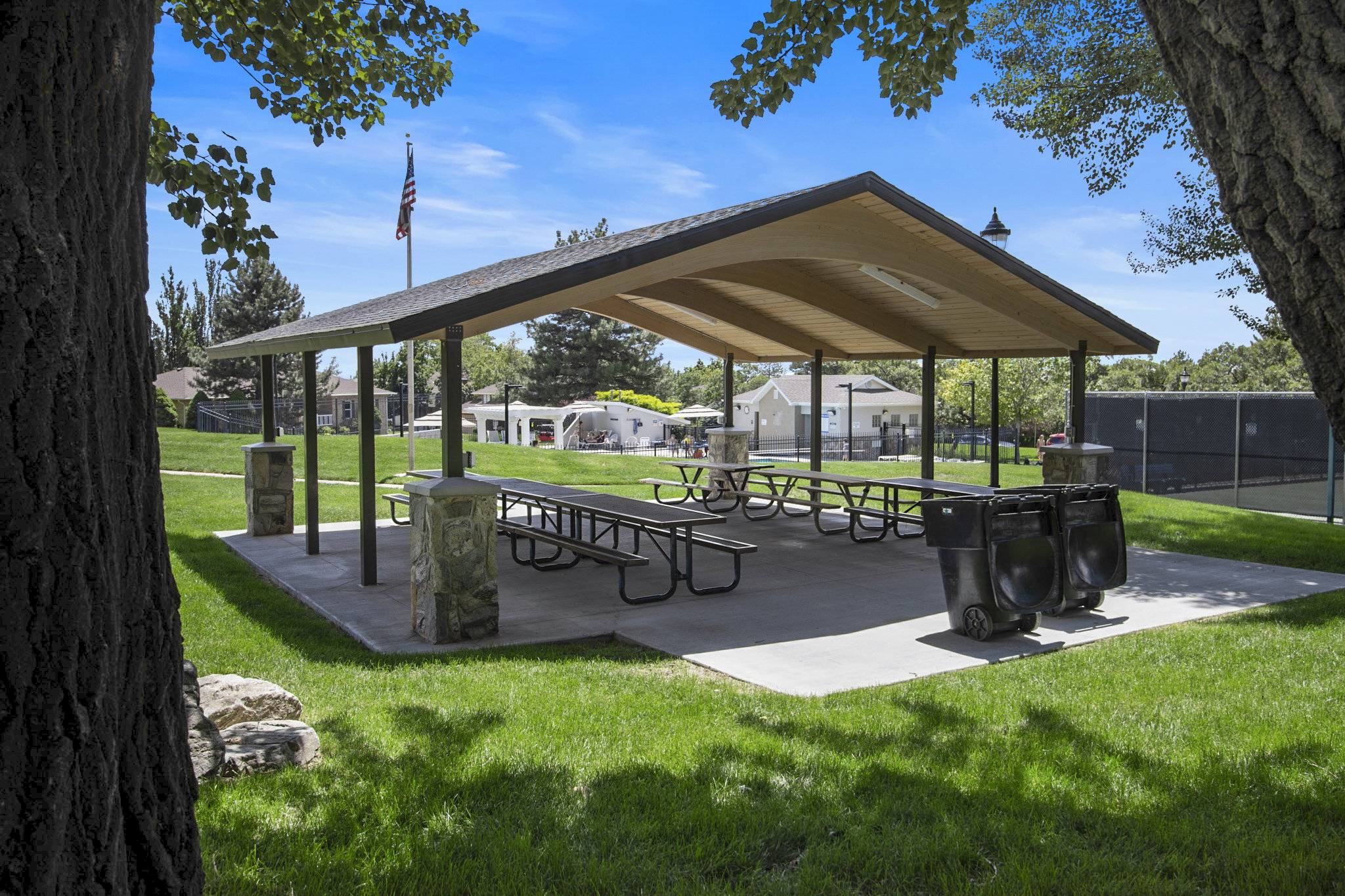 Covered pavilion with stone-accented columns, multiple picnic tables, and a concrete pad