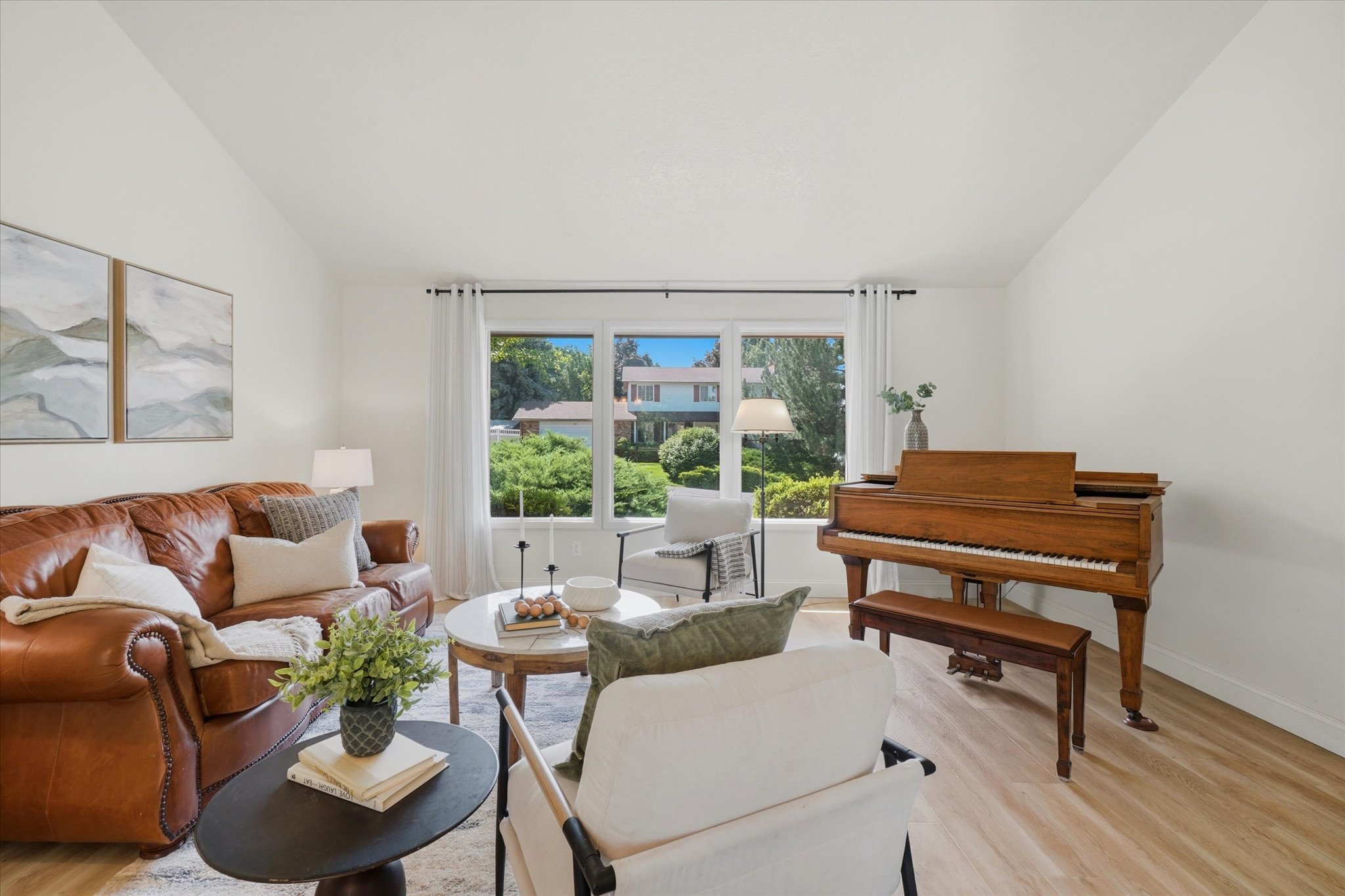 Bright living area with high ceilings, wood-finish flooring, and a large picture window