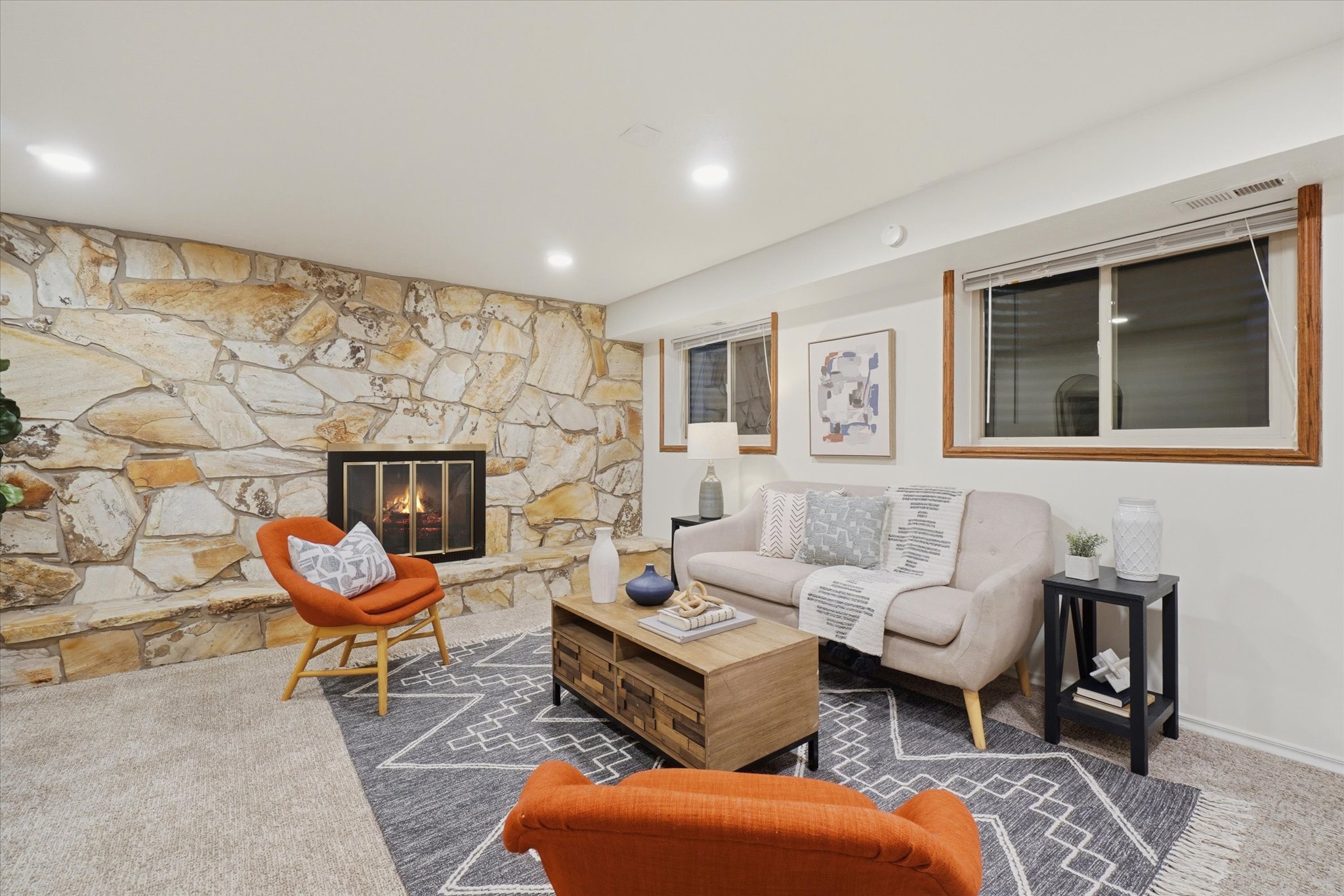 Living area featuring a floor-to-ceiling natural stone fireplace with a raised hearth, recessed lighting, wood-trimmed windows, and light-toned carpeting