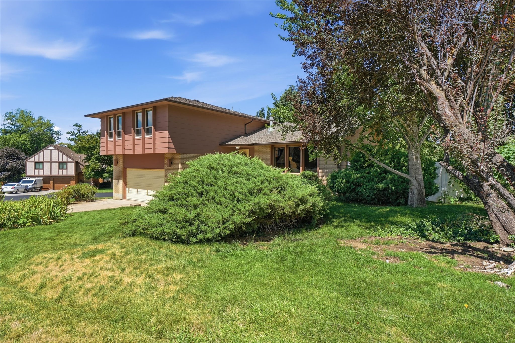 Split-level residence featuring a two-car garage, partial siding, and prominent front windows