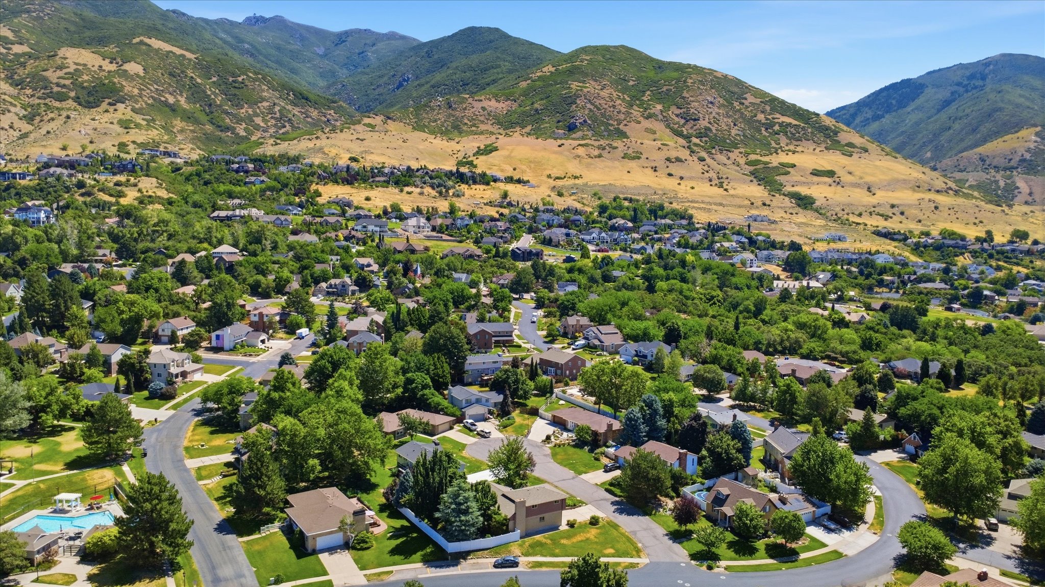 Expansive residential area featuring numerous homes nestled among mature trees, with prominent mountain terrain providing a scenic backdrop
