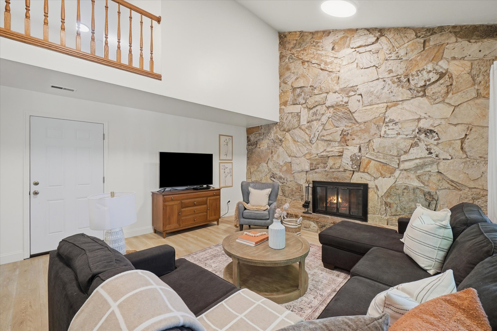 Living area featuring a floor-to-ceiling stone fireplace, high ceilings, wood-finish flooring, and an upper-level balcony with wood railing