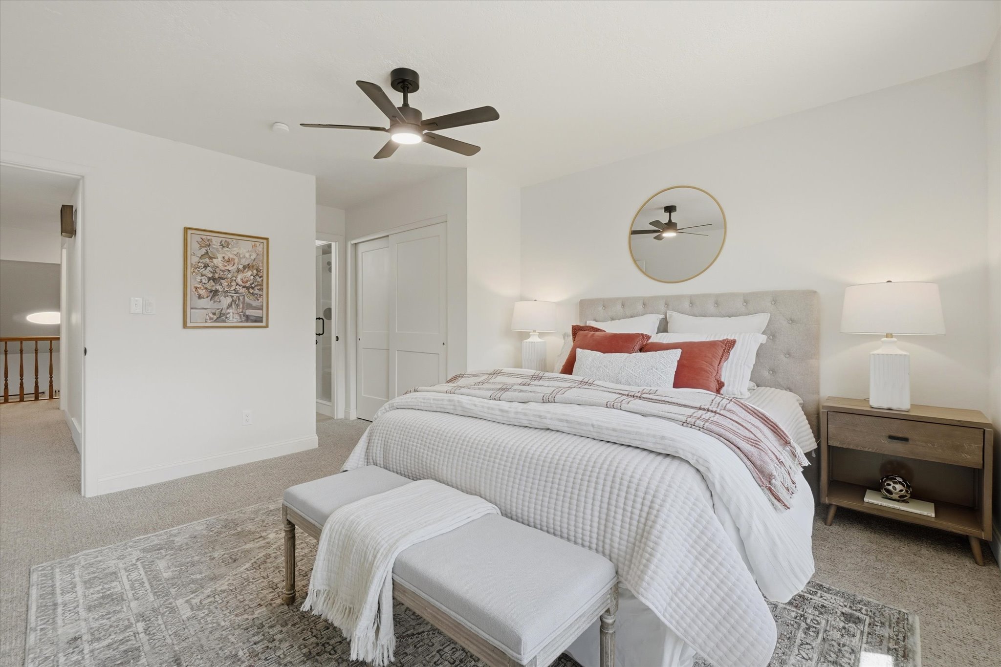 Carpeted bedroom featuring a tufted headboard, a ceiling fan with integrated lighting, white walls, a sliding closet door, and a partially visible bathroom entrance