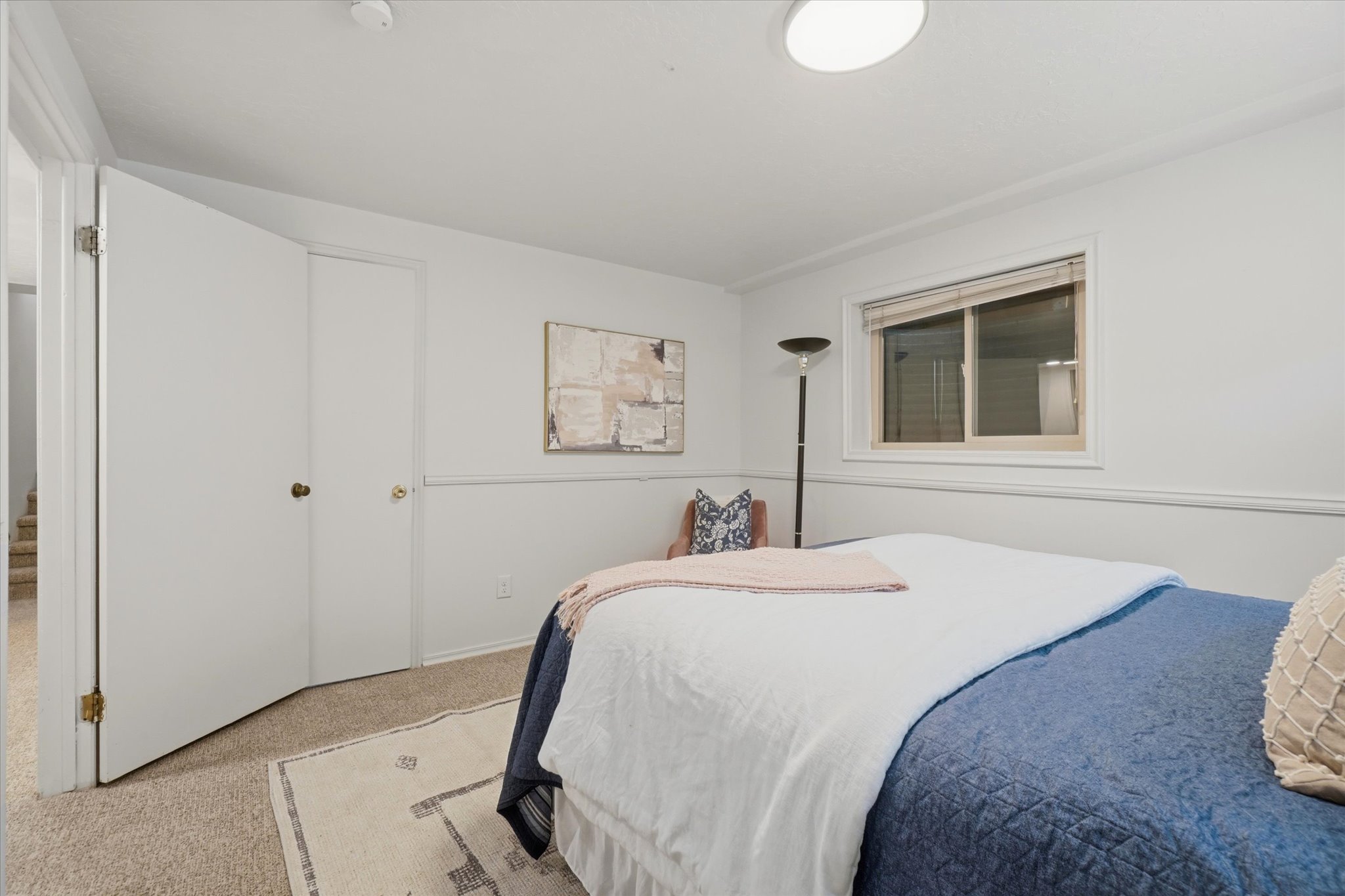 Carpeted room featuring a window with blinds, white walls, and a built-in closet with bifold doors