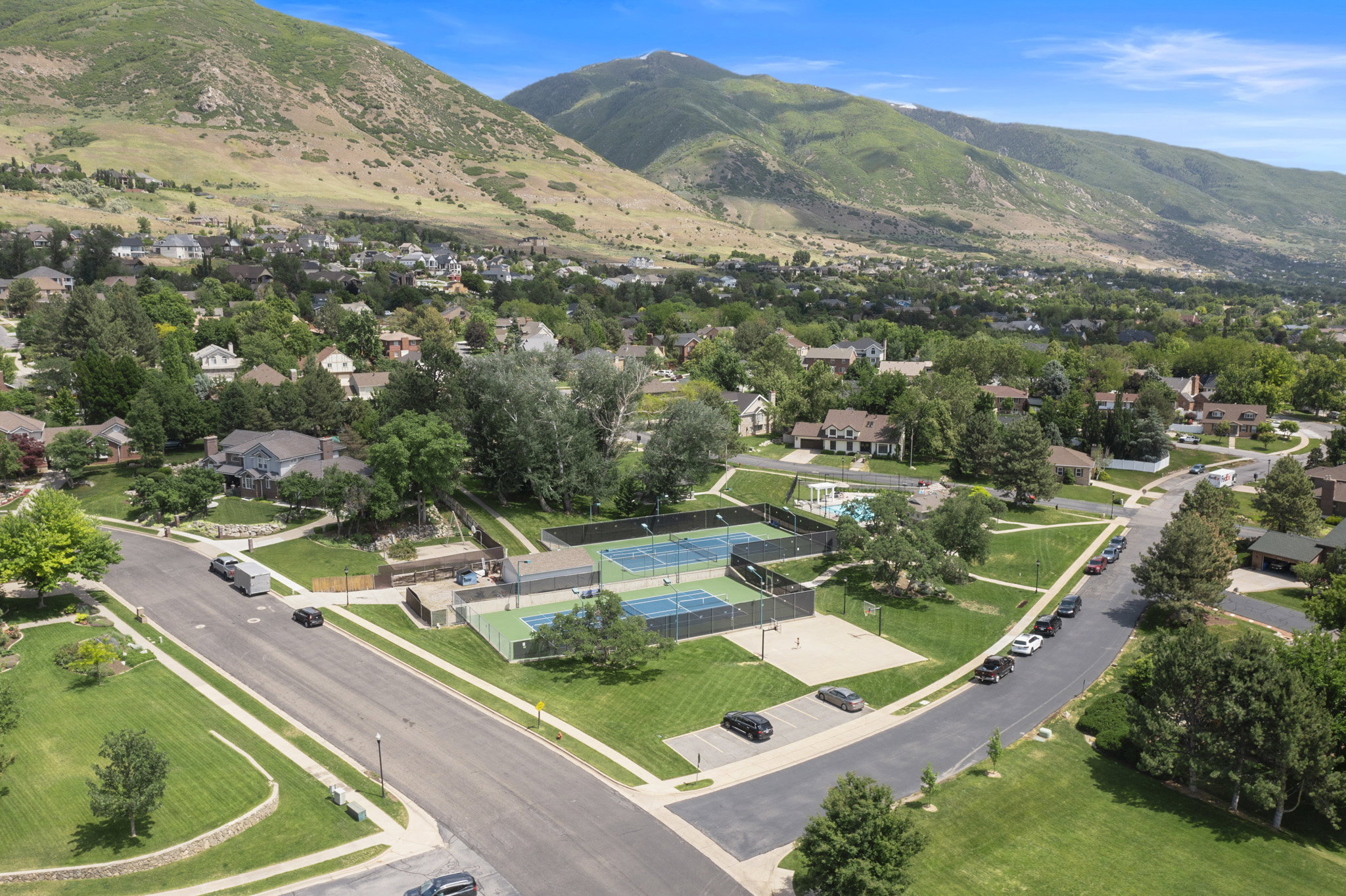 Community green space featuring two tennis courts, an additional sport court, and a swimming pool, all surrounded by mature trees