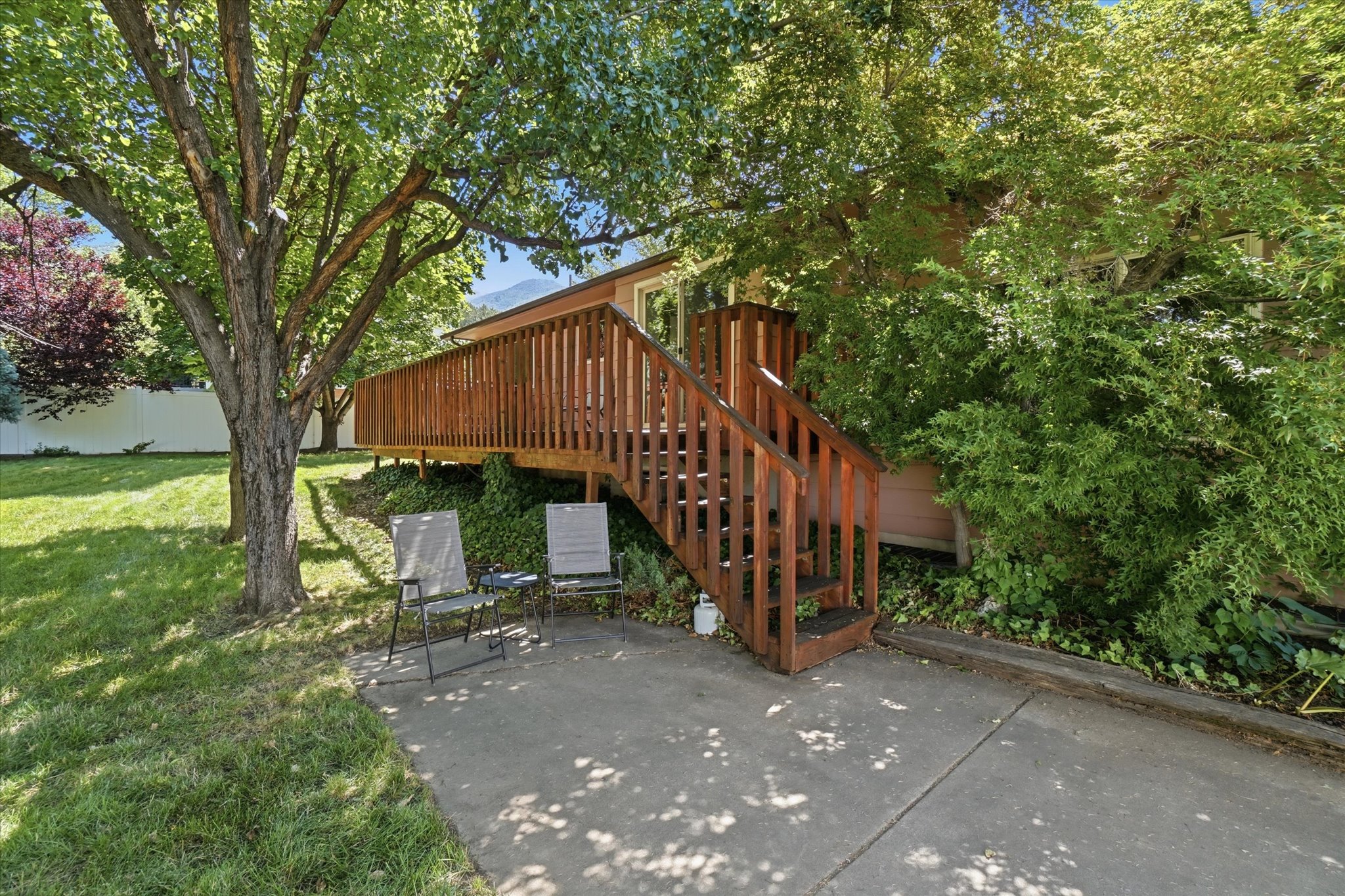 Elevated wood deck with railings and stairs, a concrete patio area, and a lush green lawn