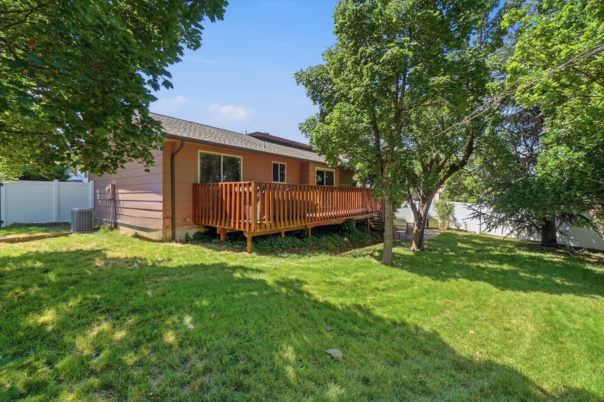 Expansive backyard featuring a wood deck, sliding glass door access, mature trees, and a white privacy fence