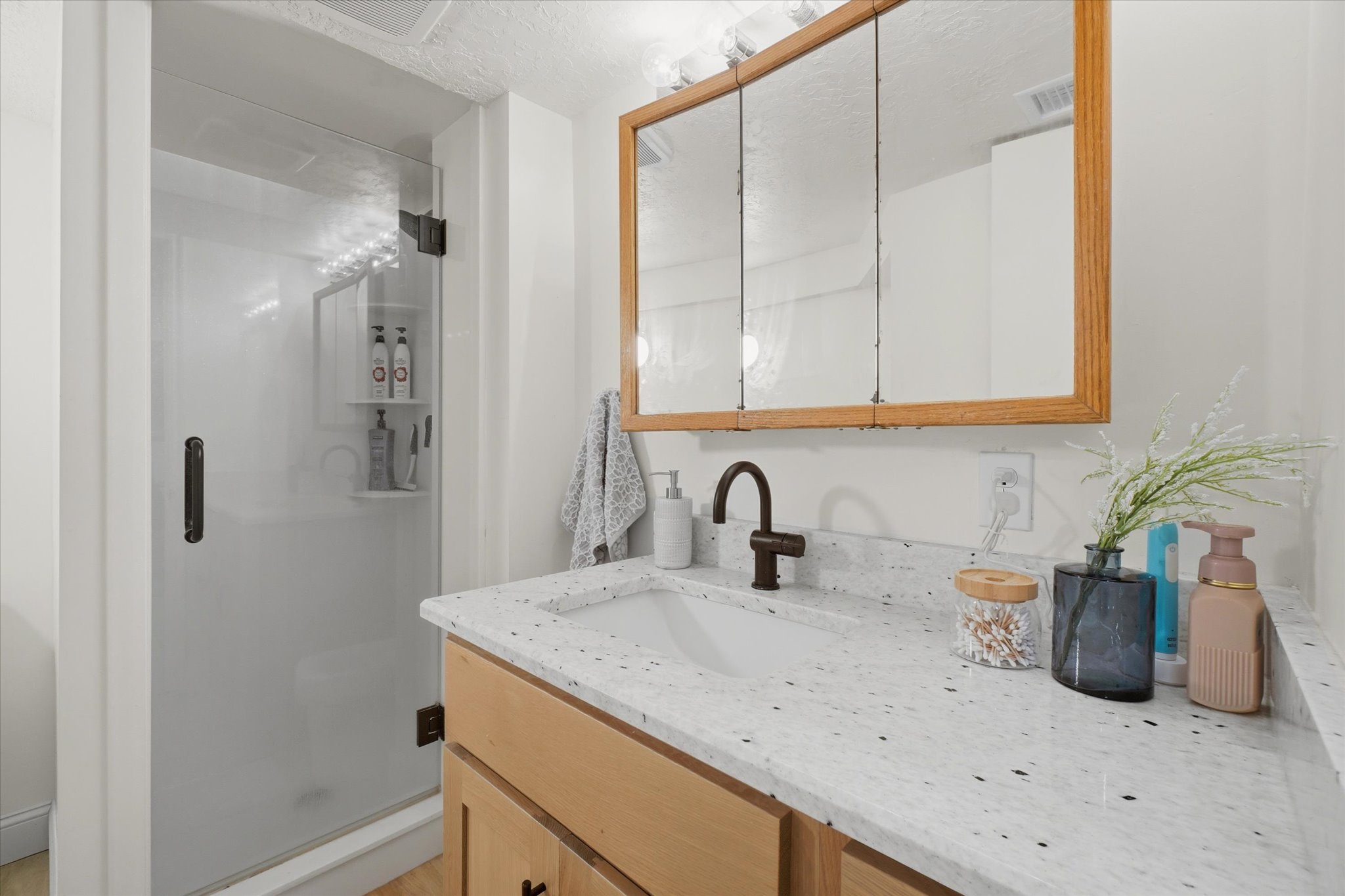 Bathroom featuring a glass-enclosed shower, light wood vanity, white countertop with integrated sink, and an overhead mirror with wood trim