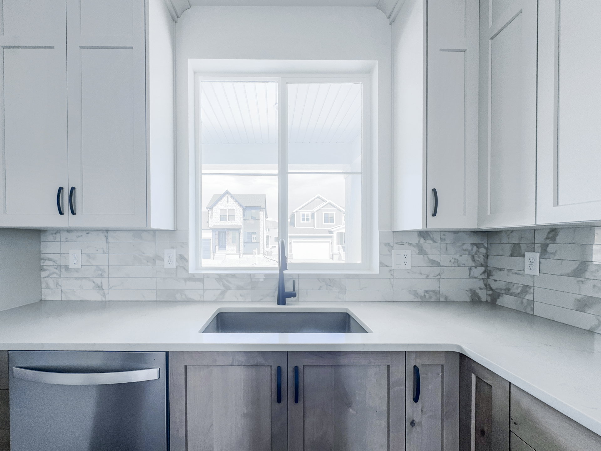 Kitchen featuring a stainless steel undermount sink, a matte black faucet, light countertops, and a white subway tile backsplash