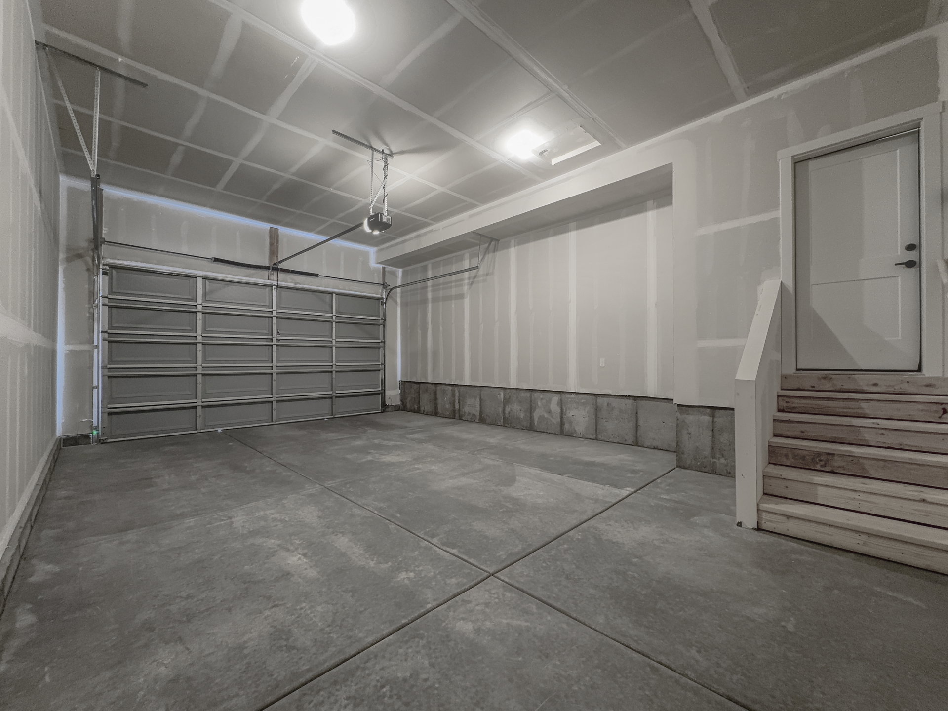 Spacious garage featuring concrete flooring, a paneled garage door, and a dedicated entry door with wooden steps and railing